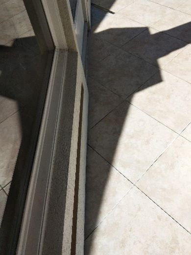 Sliding glass door beside sunlit tiled patio with strong shadows