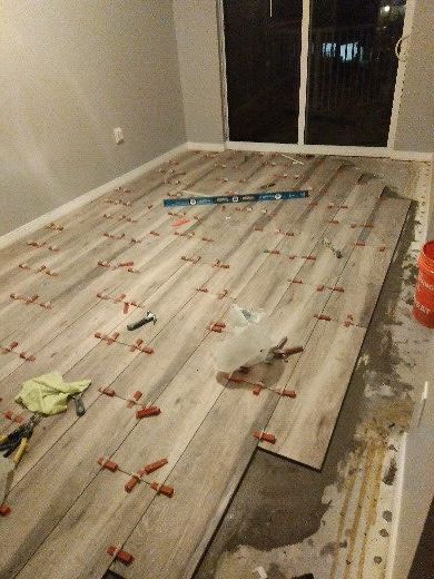 Partially installed gray wood-look flooring in an empty room, with tools and spacers visible.