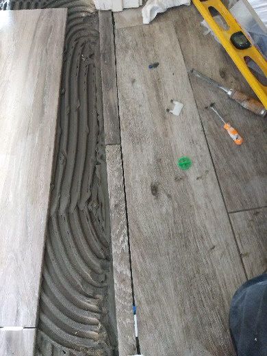 A tiled floor with fresh mortar ridges, a yellow level, and scattered tools during installation աշխատանք