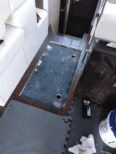 Narrow boat cabin aisle with metal floor panel, white seating, and cleaning supplies on the floor