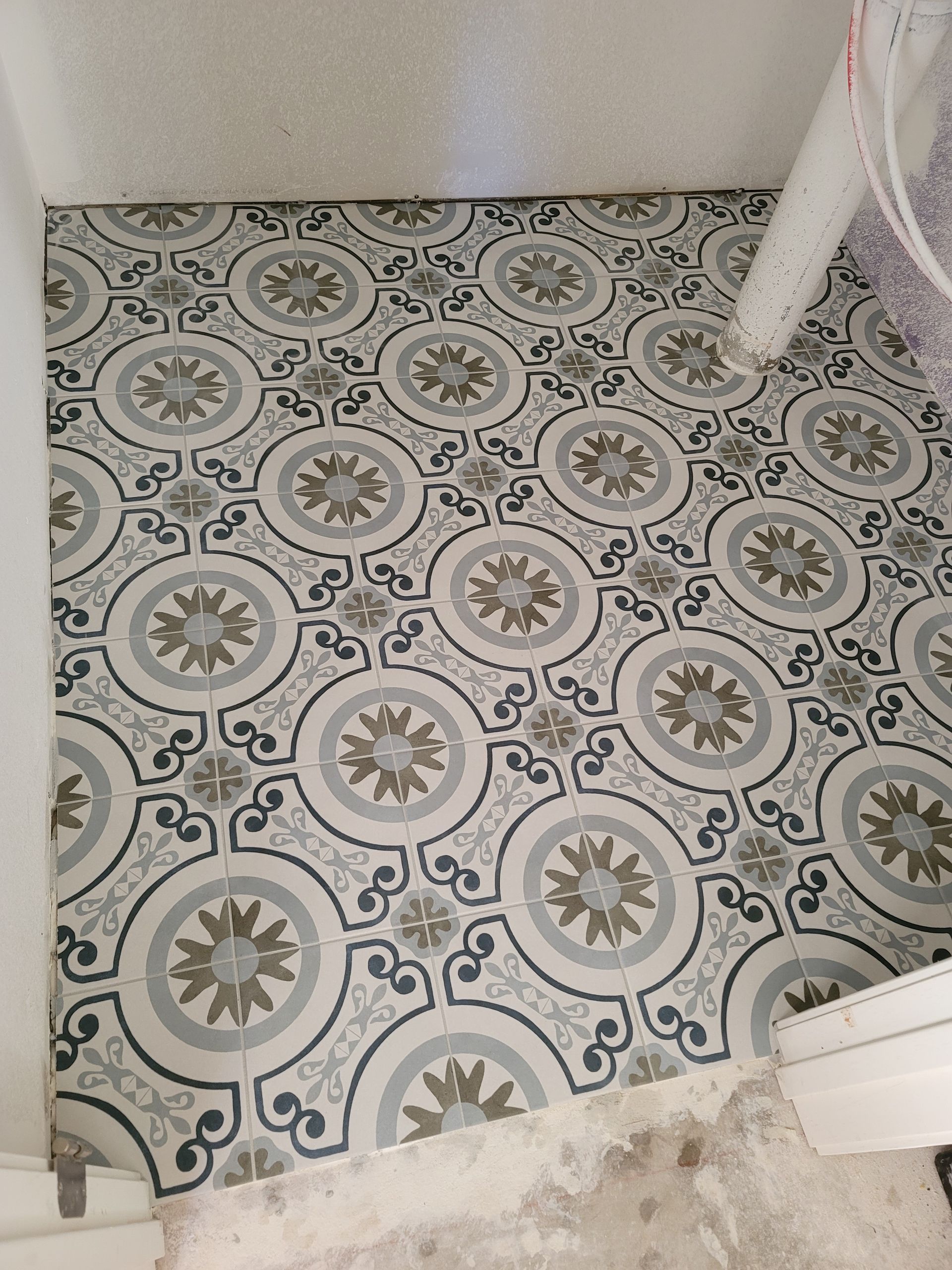 Patterned tile floor in a small room, with white walls and a chair leg at the right edge