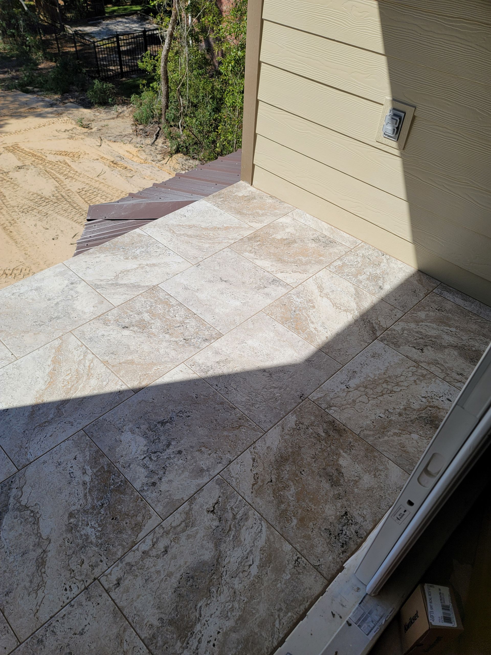 Concrete patio beside beige house wall, with sunlight and tree shadows.