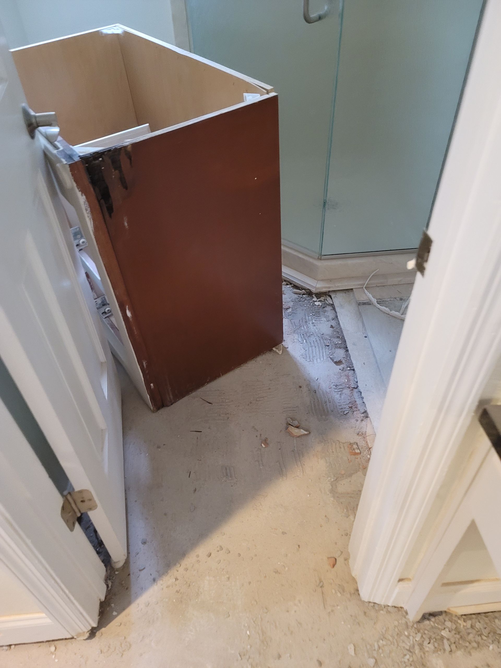 Damaged cabinet leaning in a narrow doorway, with debris scattered on the floor.