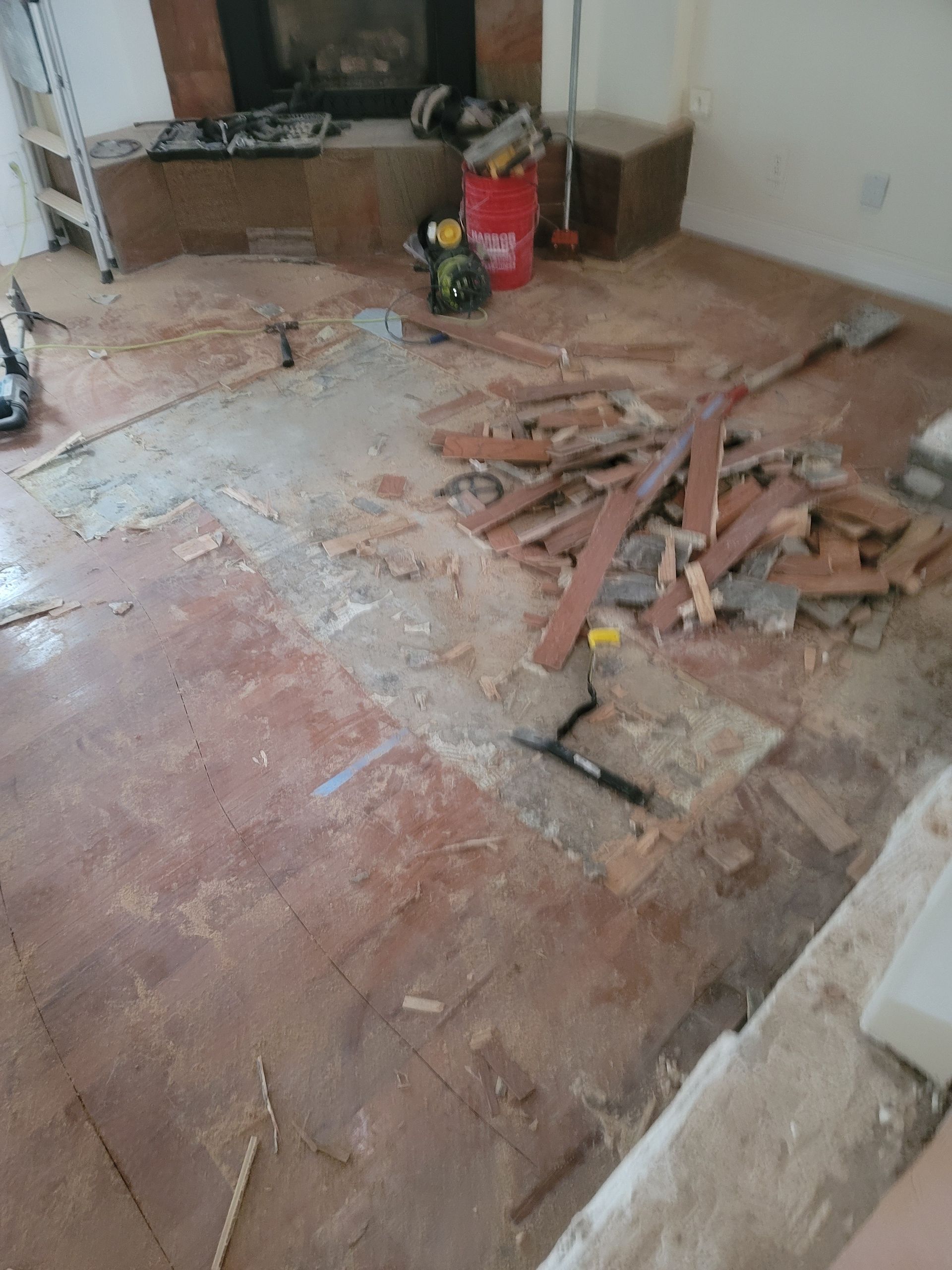 Damaged room floor with exposed wood debris and a red fire extinguisher near the wall