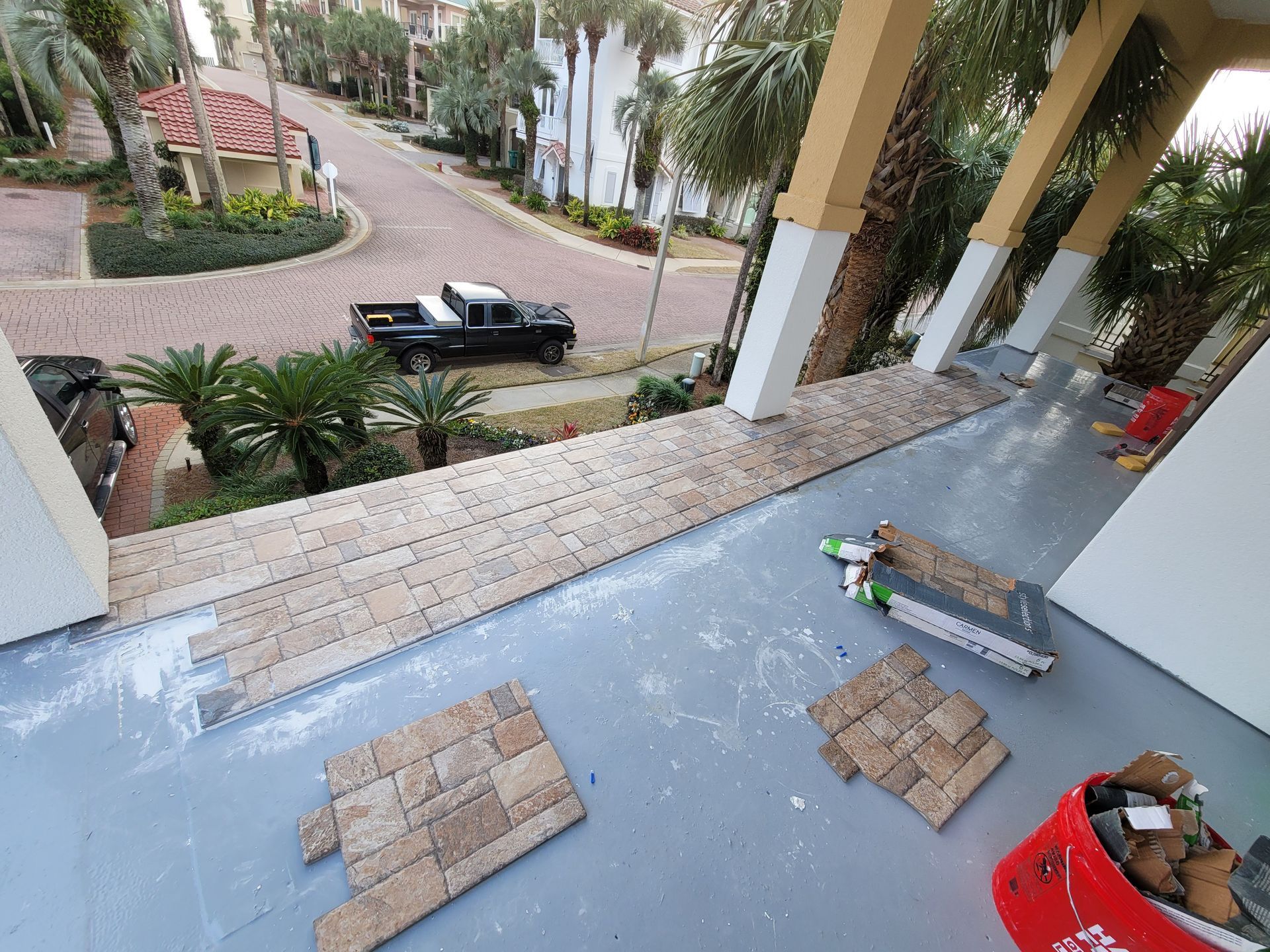Front porch under construction with tile piles, tools, and a truck parked on the driveway below.
