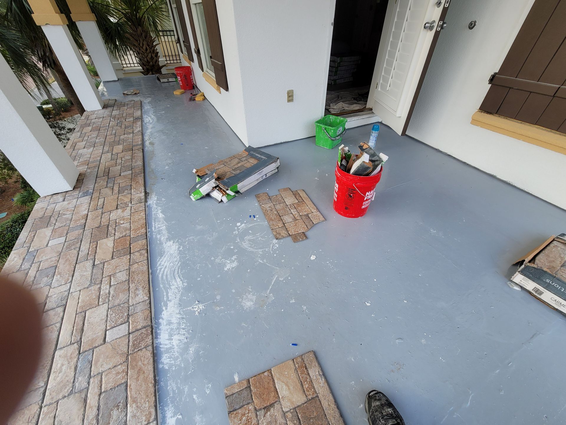 Porch under construction with paint buckets, tools, and paving materials on the floor