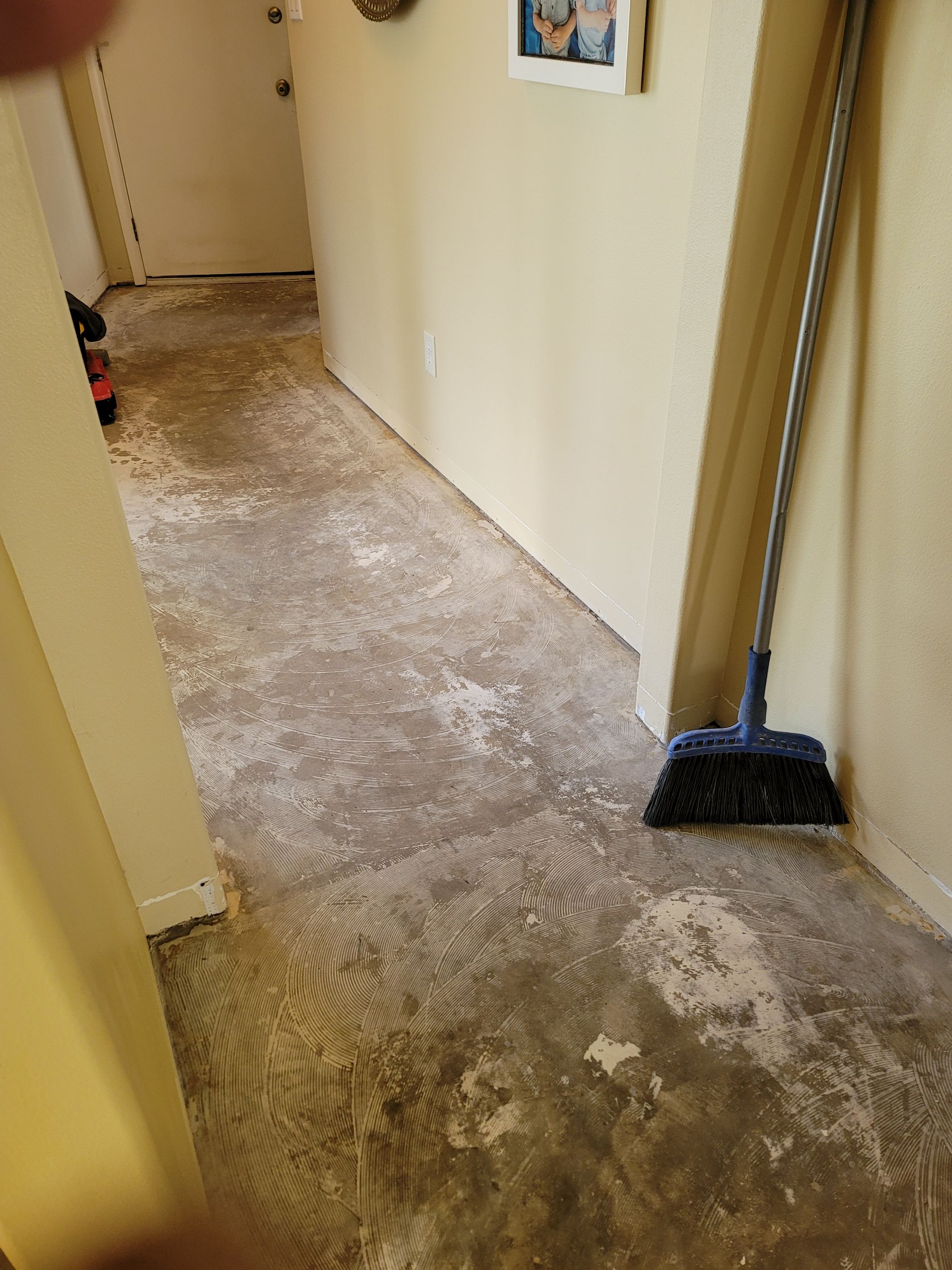 Narrow hallway with worn carpet and a broom leaning against the right wall.