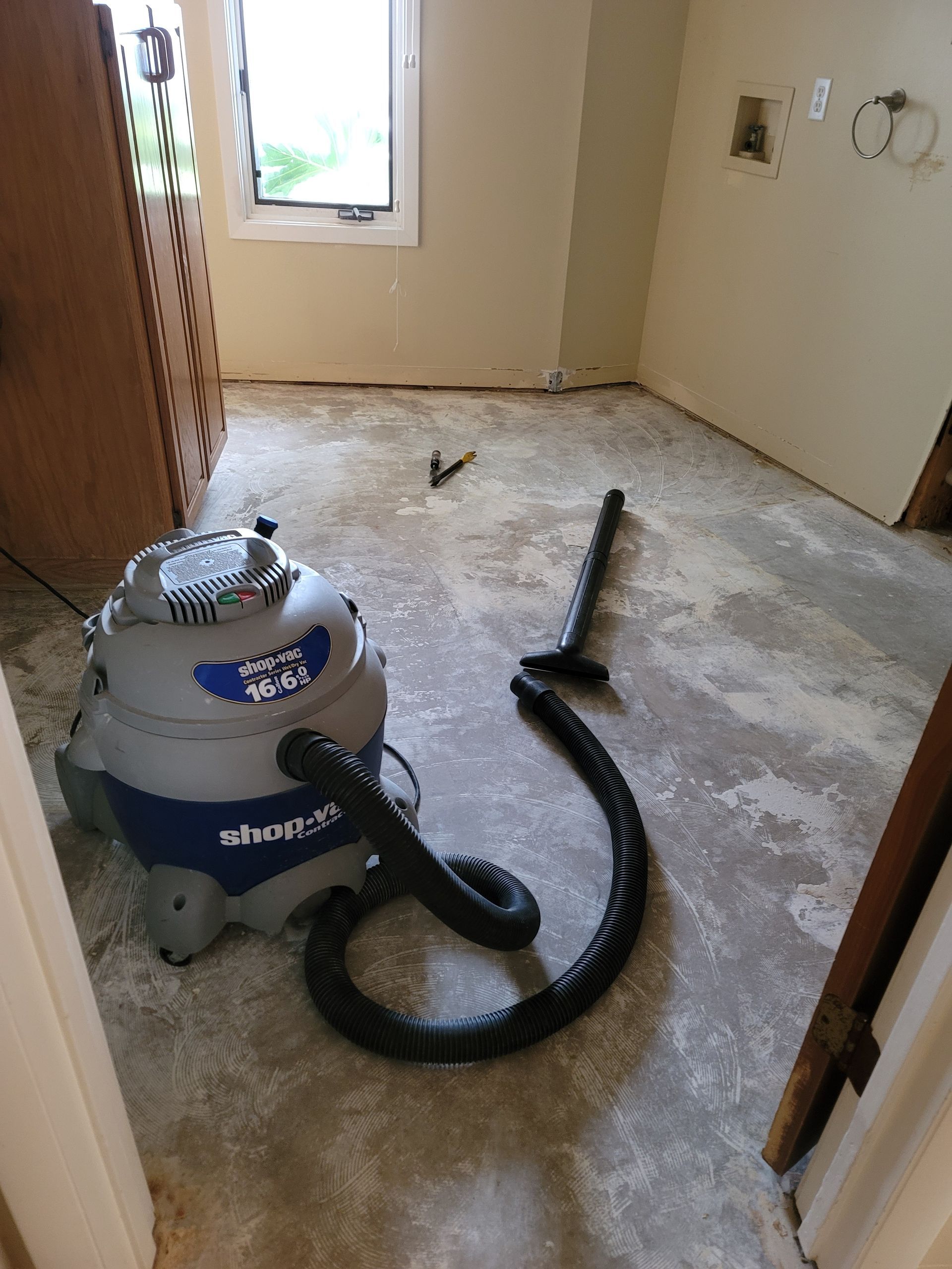 Vacuum cleaner in a dusty room with bare walls and a window.