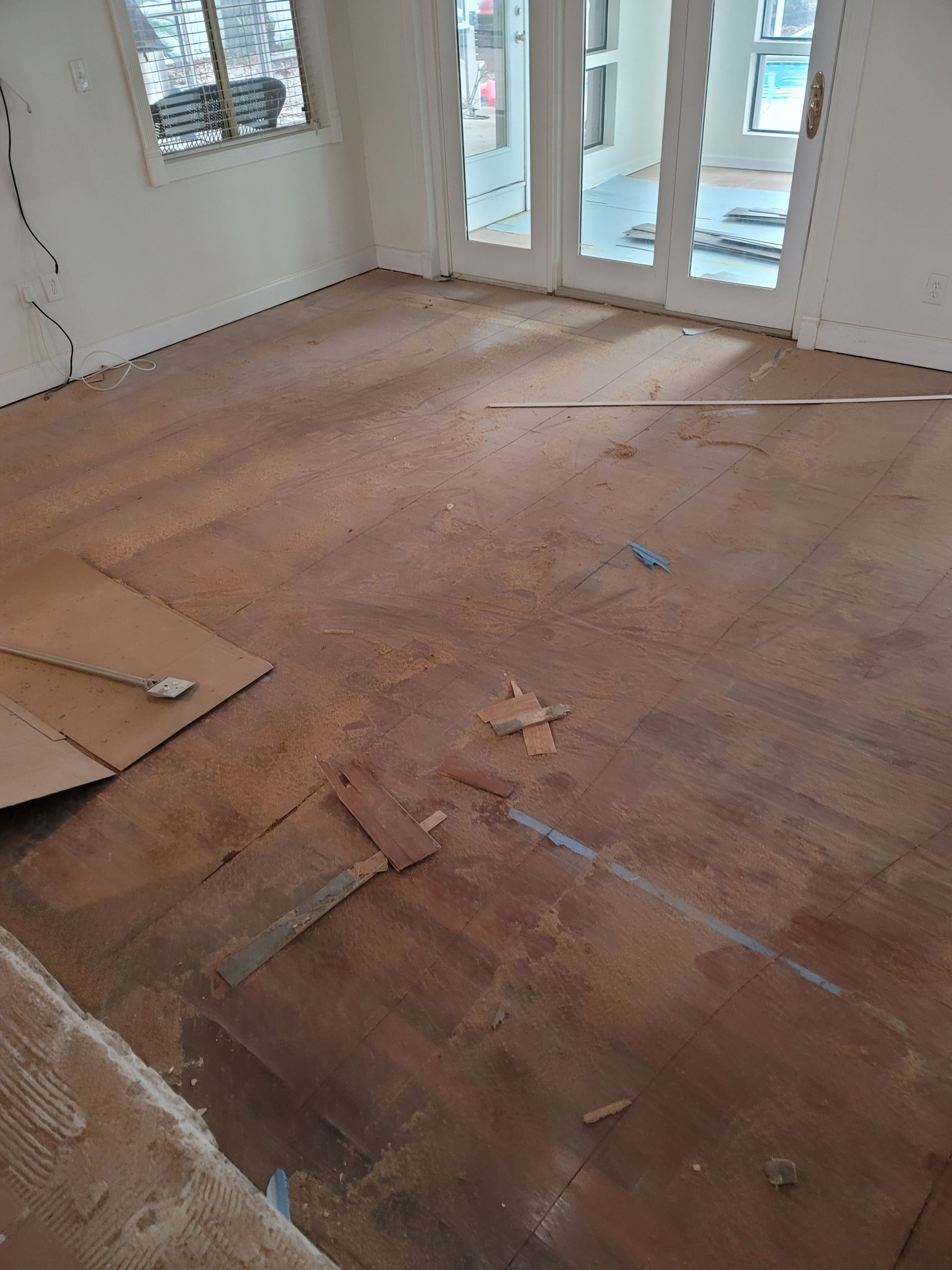 Empty room with unfinished wooden floor and large windows letting in daylight