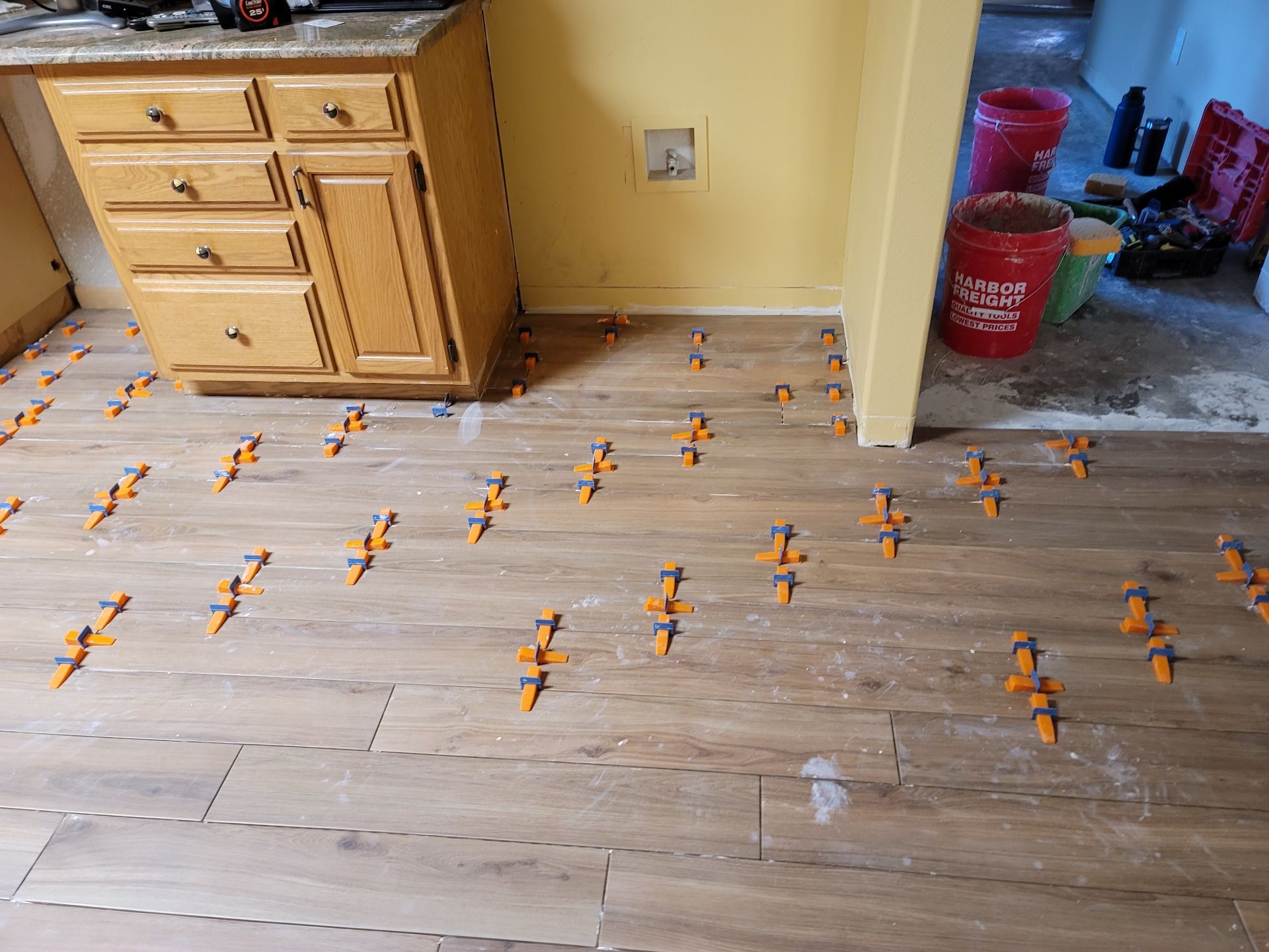 Living room floor covered with scattered orange toy airplanes beside kitchen cabinets and a doorway
