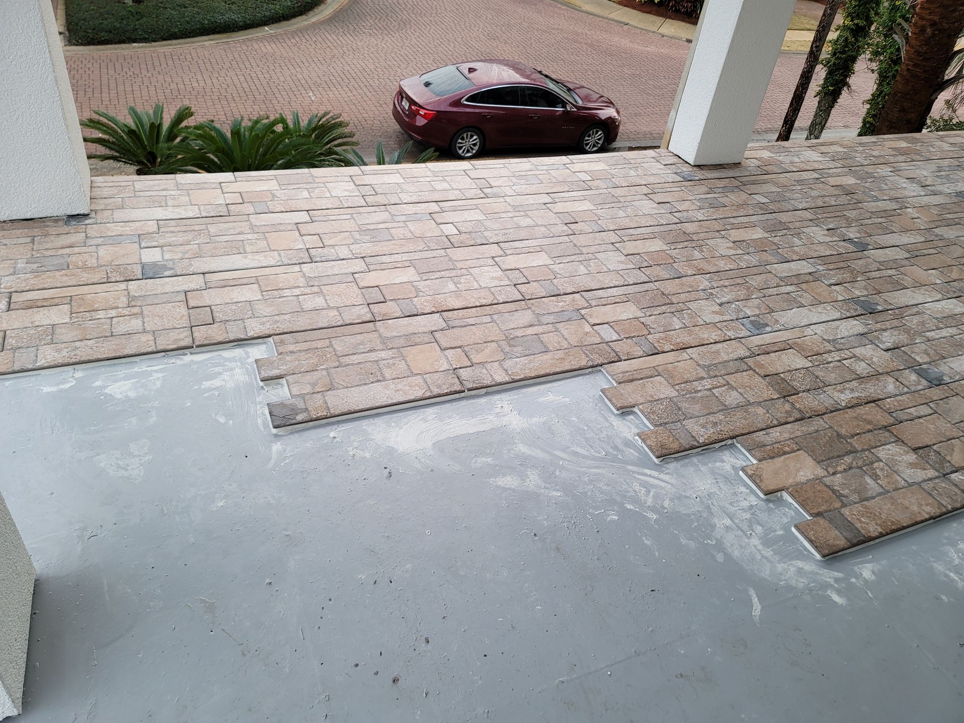 Partially finished paver walkway with a maroon car parked below on a driveway