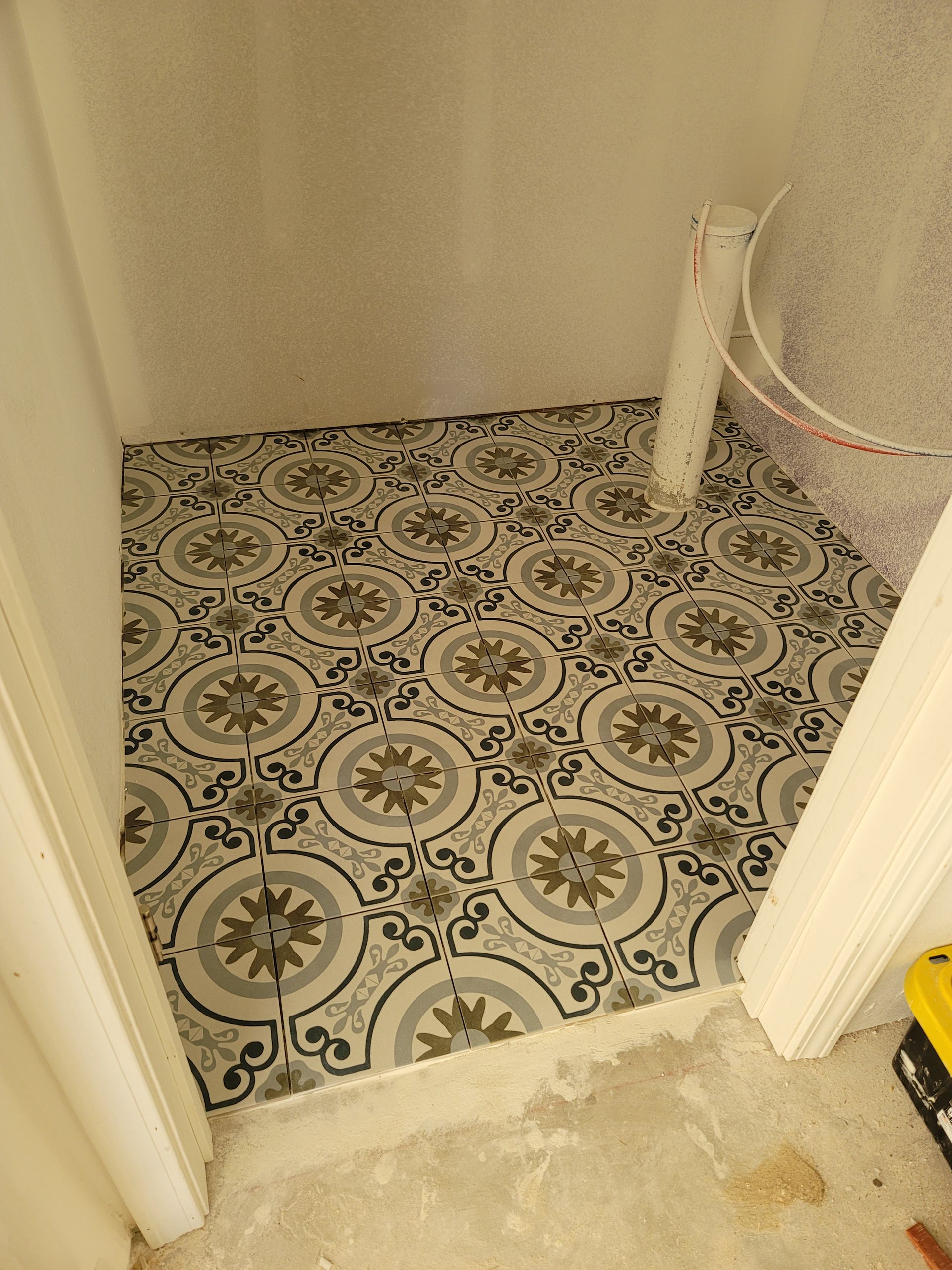 Small tiled bathroom or laundry nook with a patterned floor and unfinished concrete threshold.