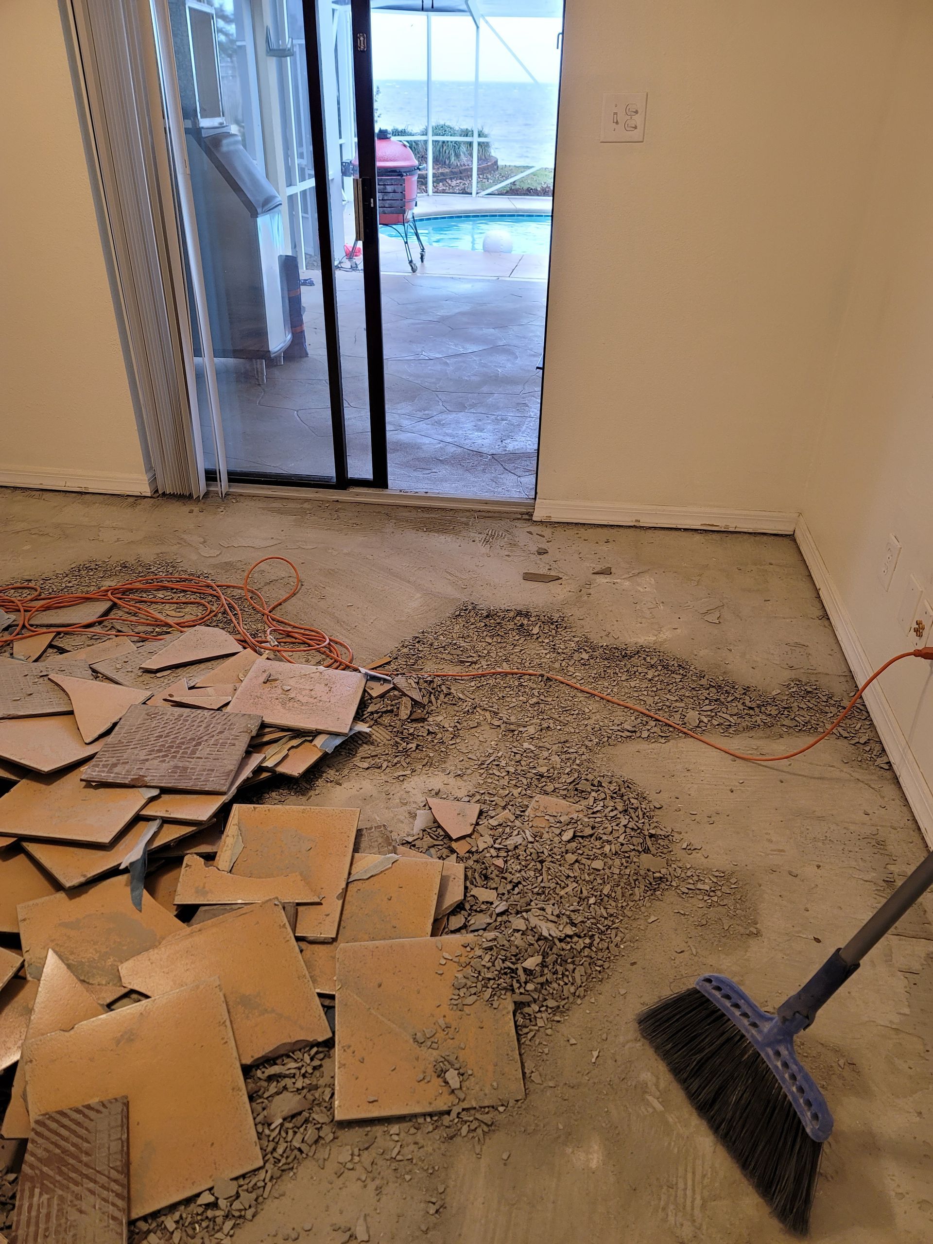 Construction debris on a floor near a doorway, with a broom and broken tile pieces scattered around.