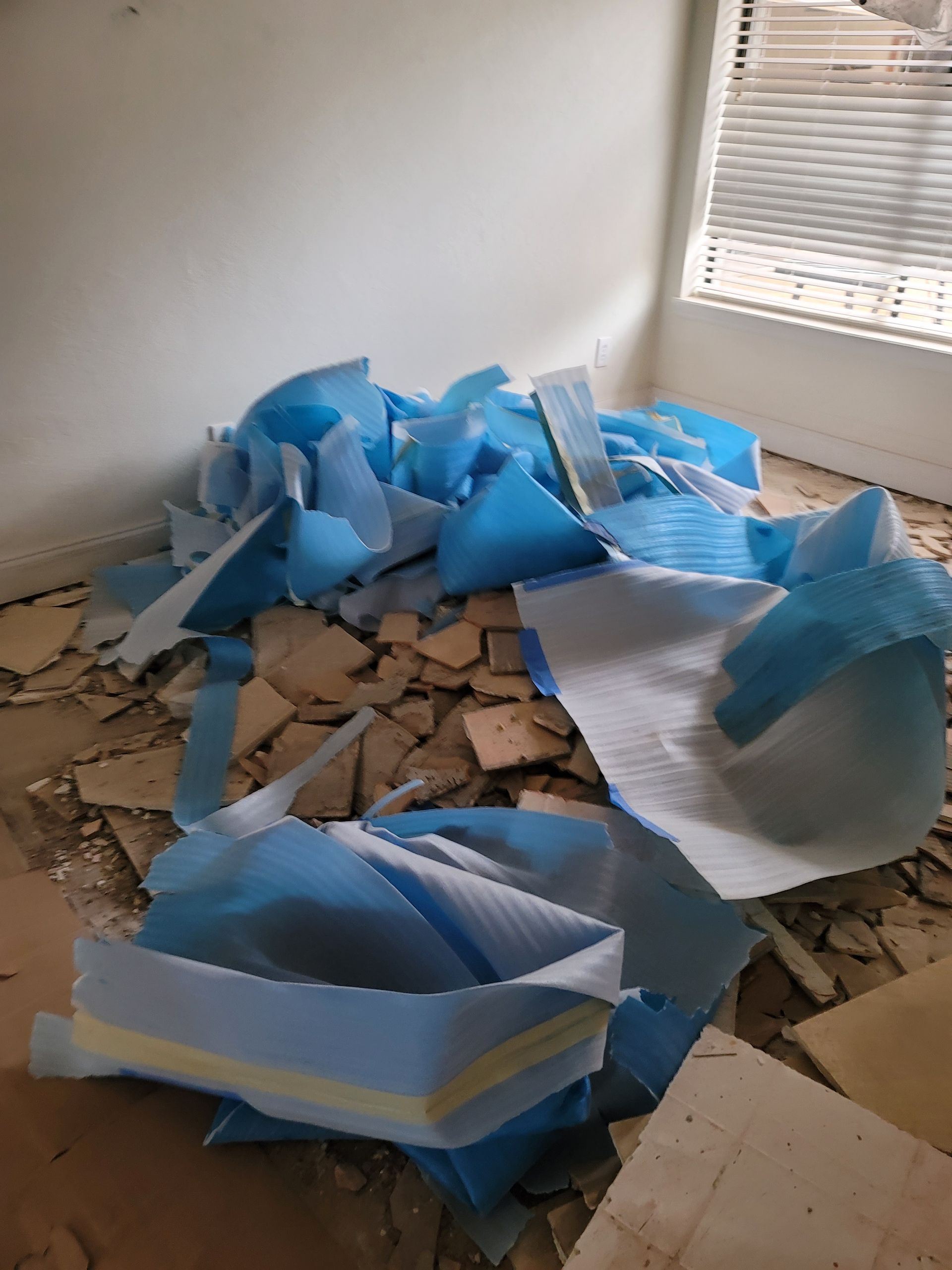Collapsed blue foam debris scattered across a damaged room floor near a window.