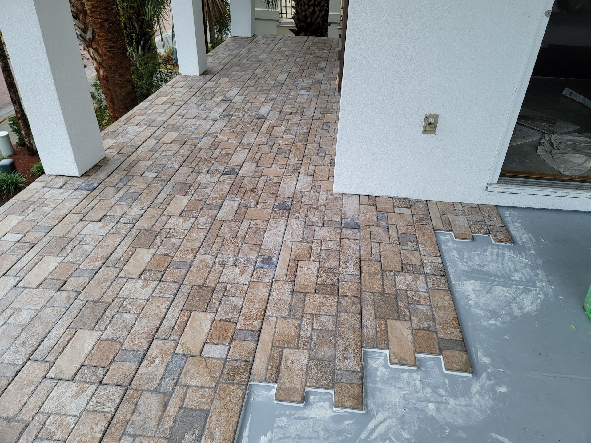 Brick patio walkway beside a white house, with unfinished concrete edge and columns