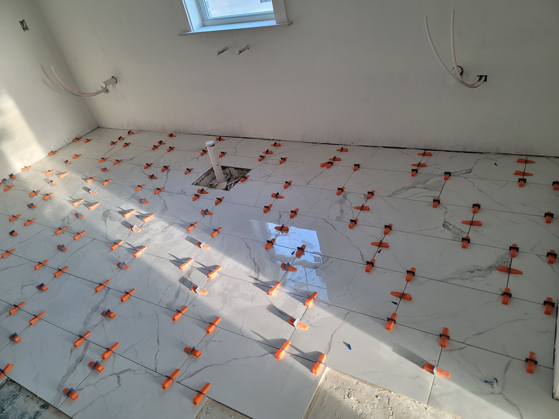Tiled floor under construction with orange spacers and sunlight streaming through windows