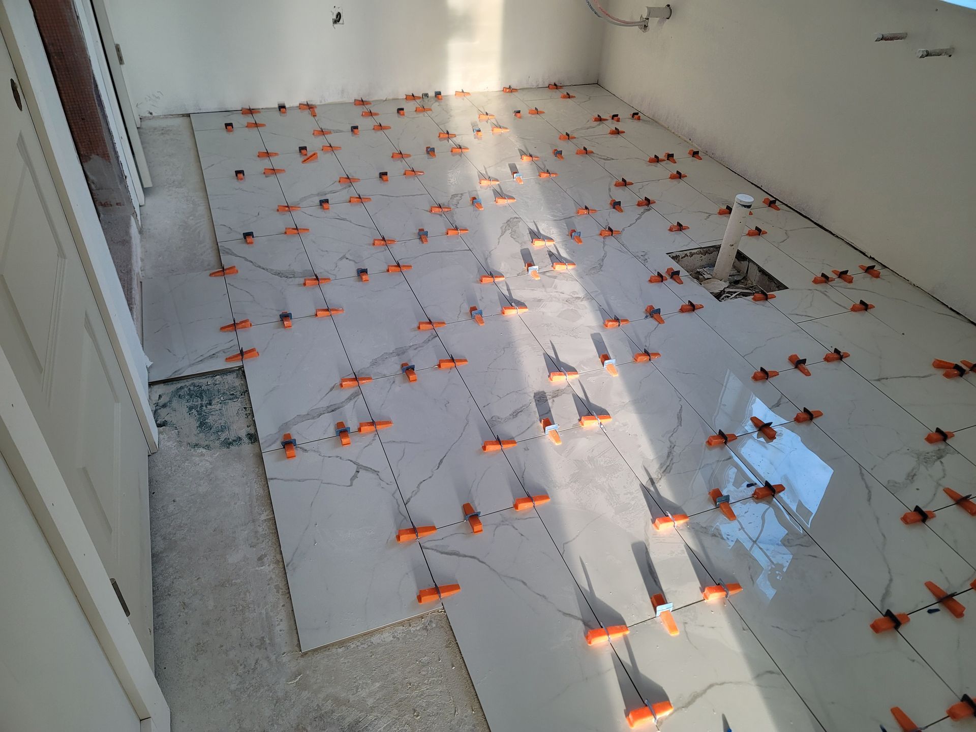 White tiled floor with orange spacers and debris in a sunlit room under construction