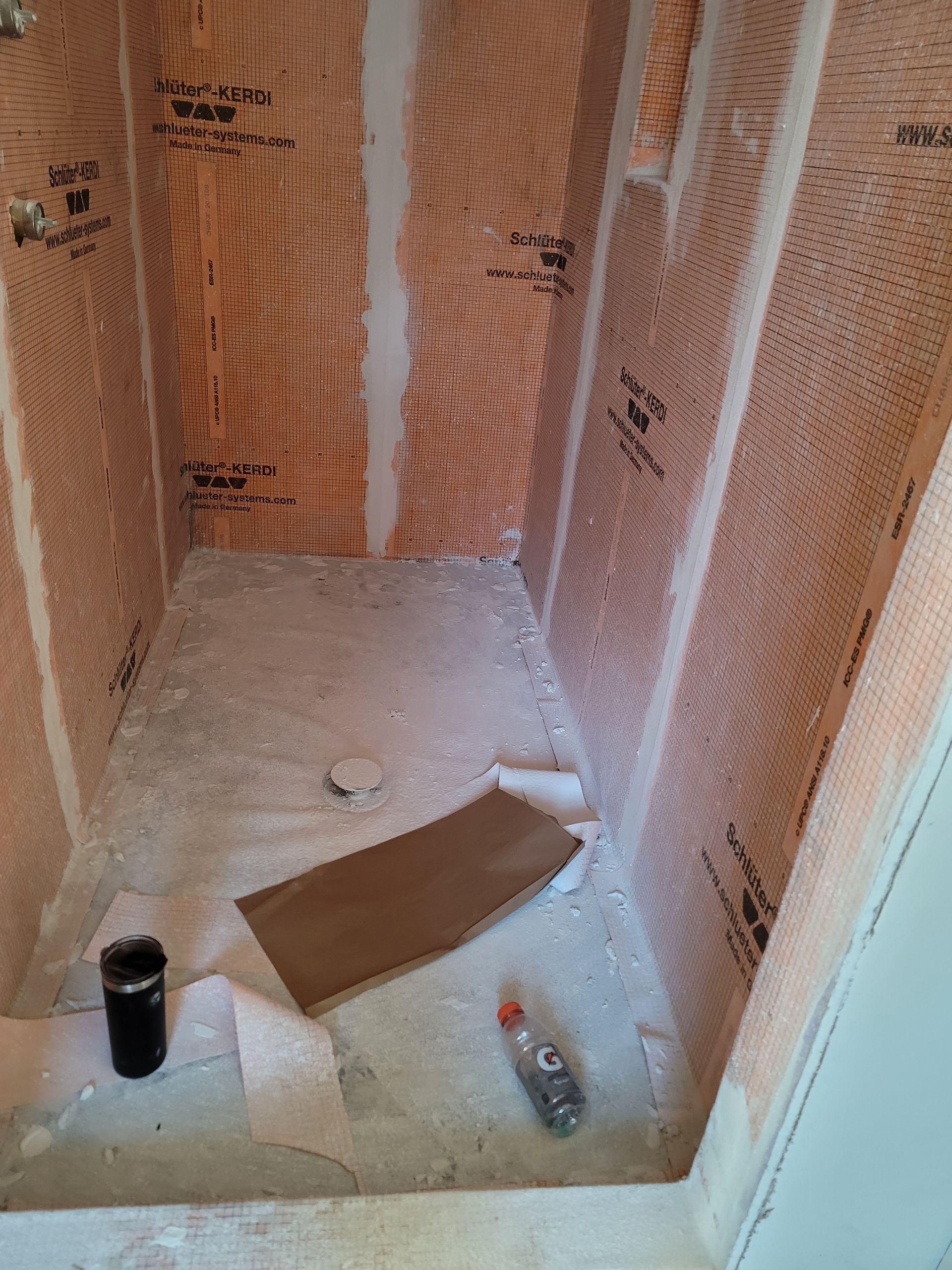 Partially tiled shower stall under construction with orange waterproofing membrane and tools on the floor