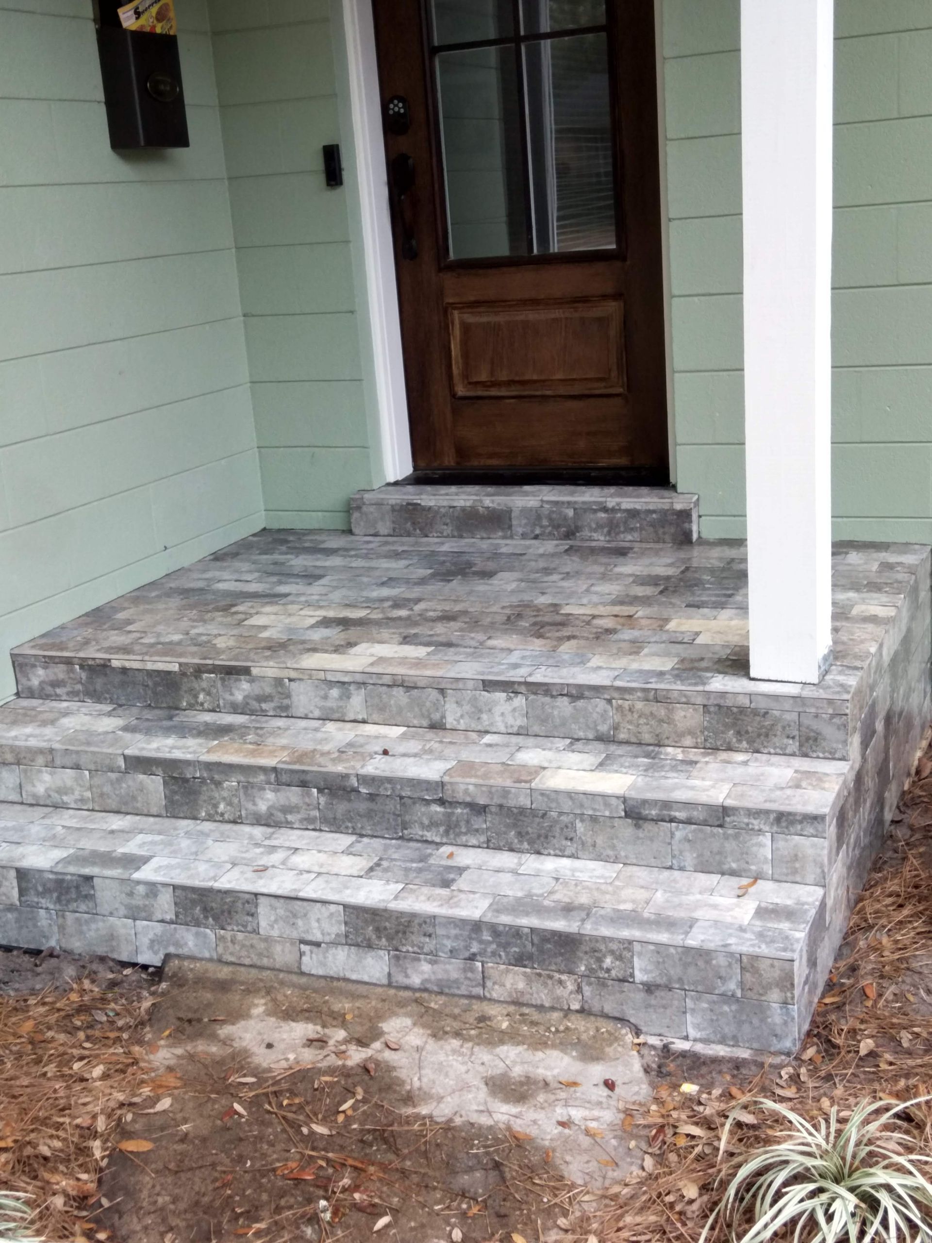 Stone front steps leading to a wooden front door on a light green house porch