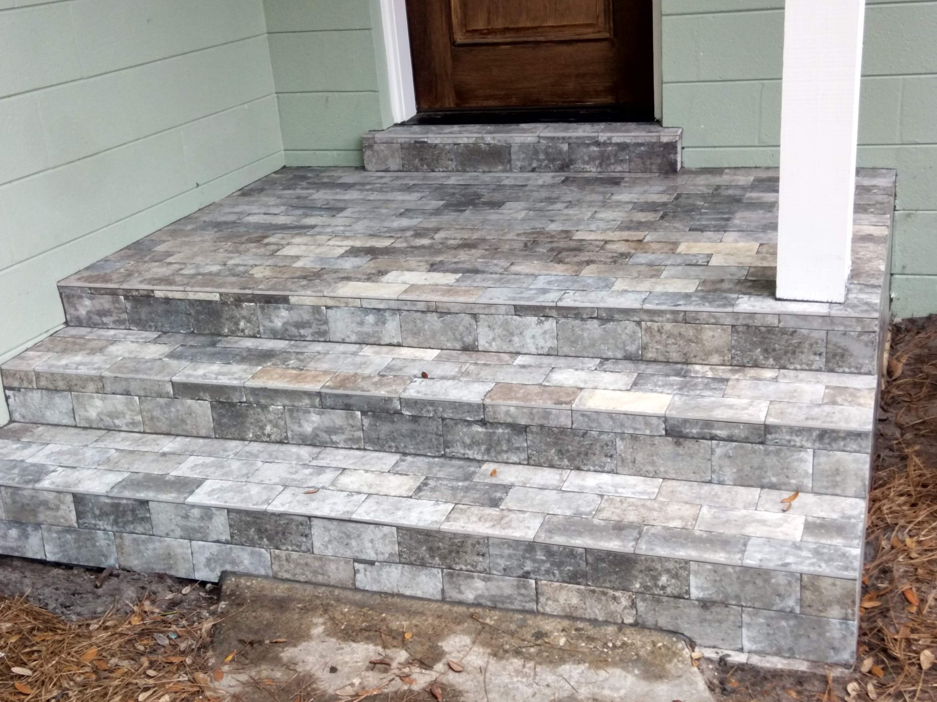 Stone front porch steps with a wooden door and white column on a light green house