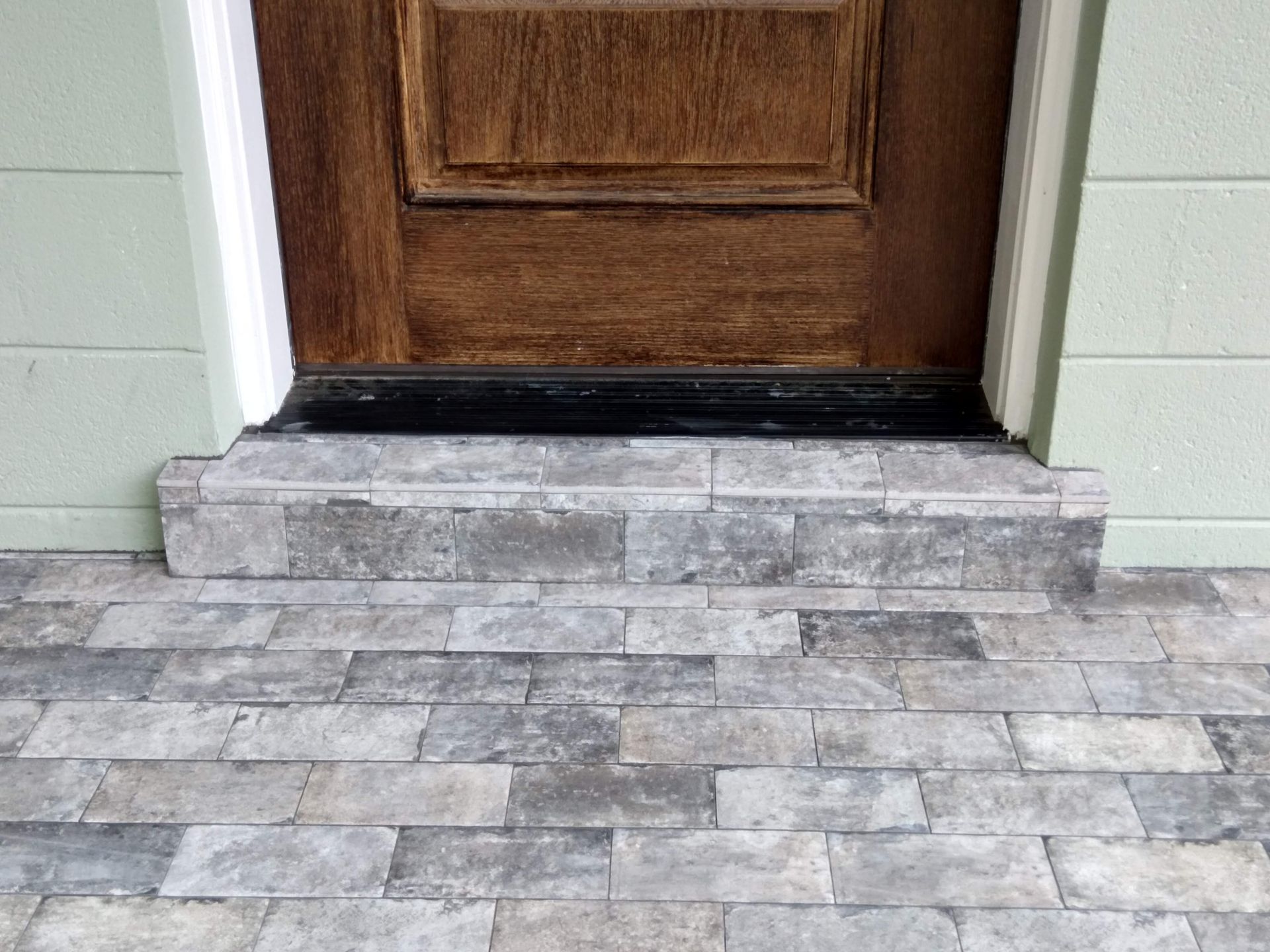 Stone front step with a wooden door above a tiled walkway
