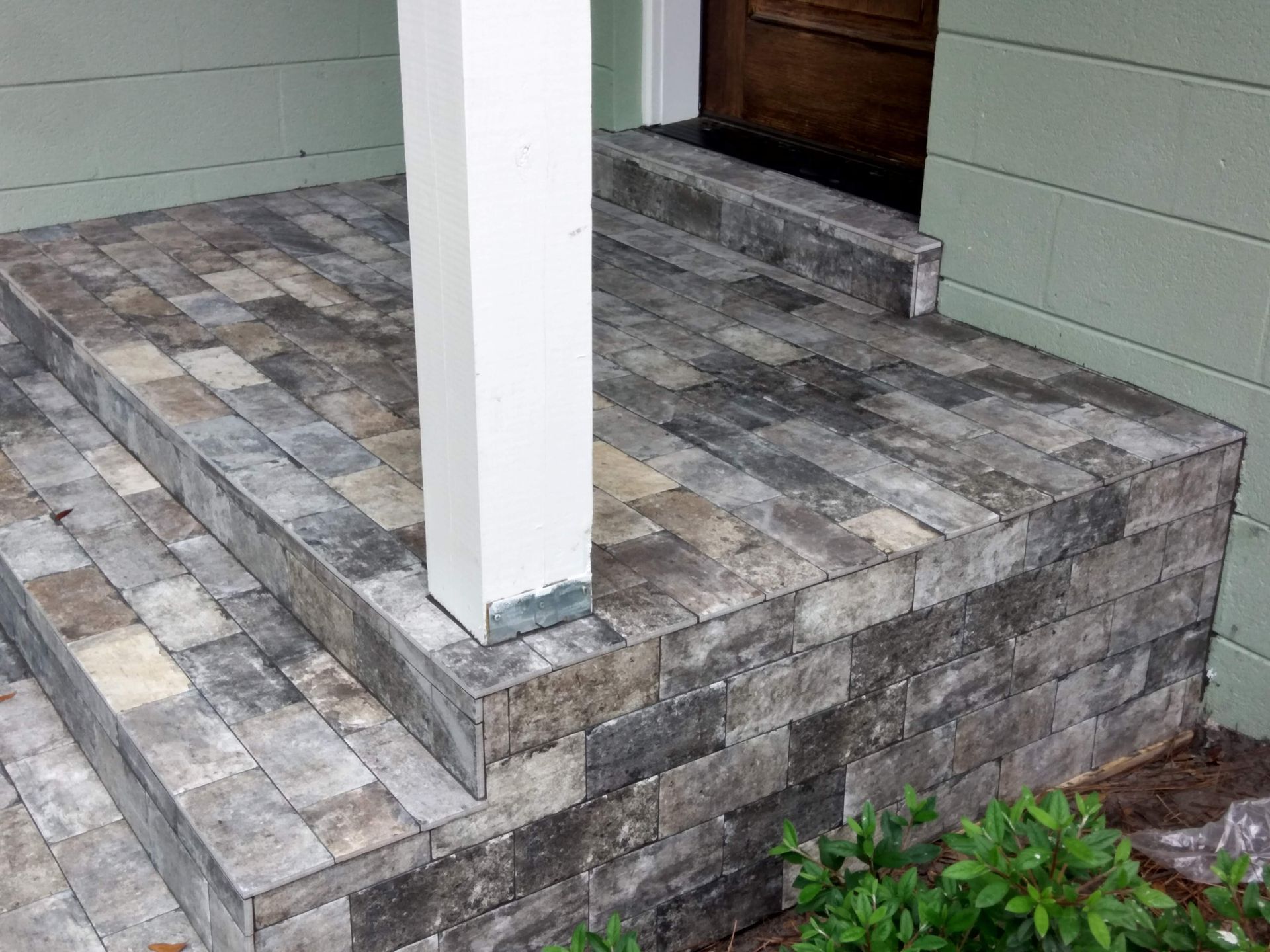 Stone-tiled front porch with a white support post and green siding beside a wooden door