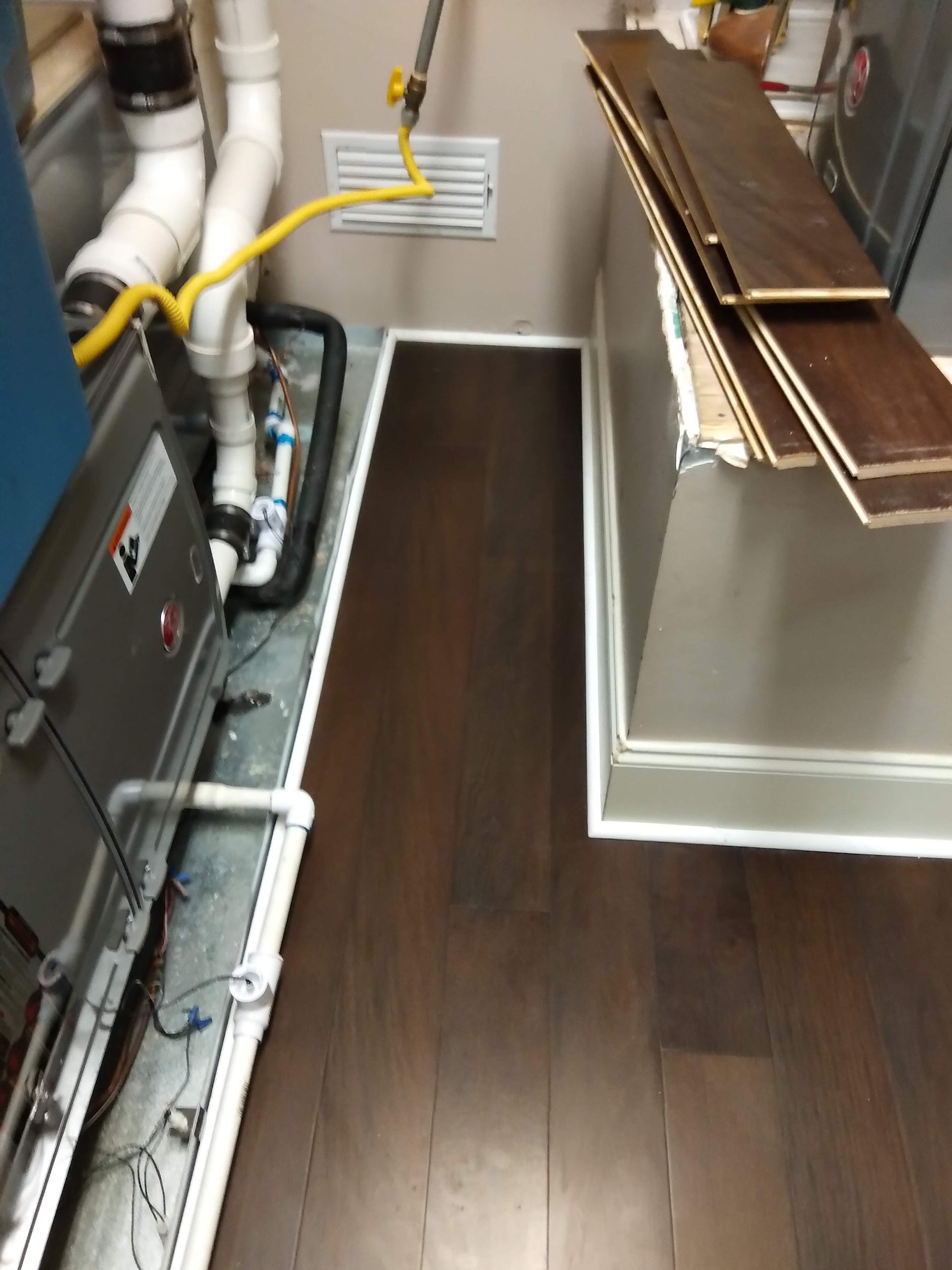 Narrow utility room with HVAC equipment, exposed pipes, and dark wood flooring beside a countertop workspace