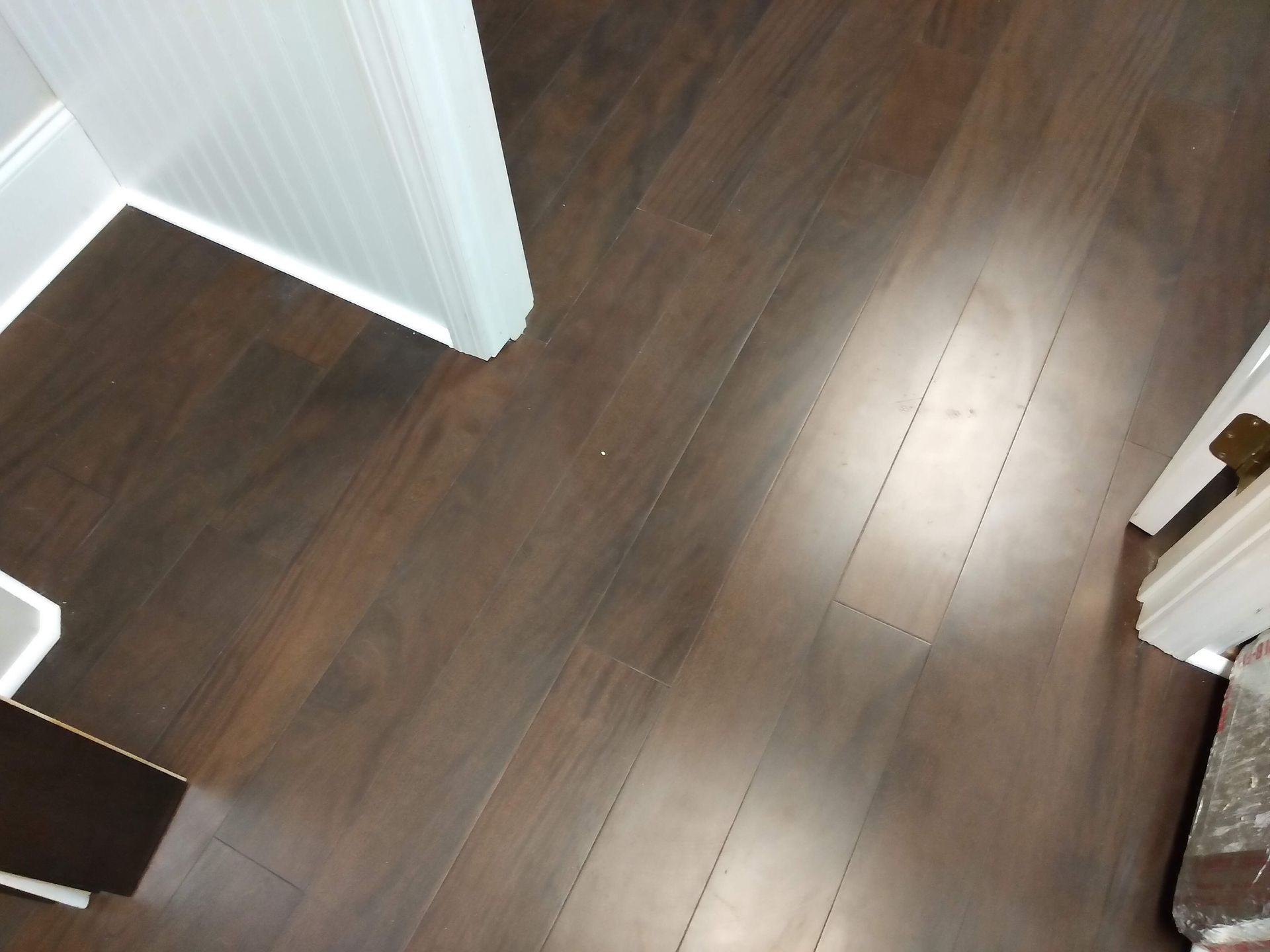 Dark wood floor in a hallway or room, with white walls and a doorway visible.