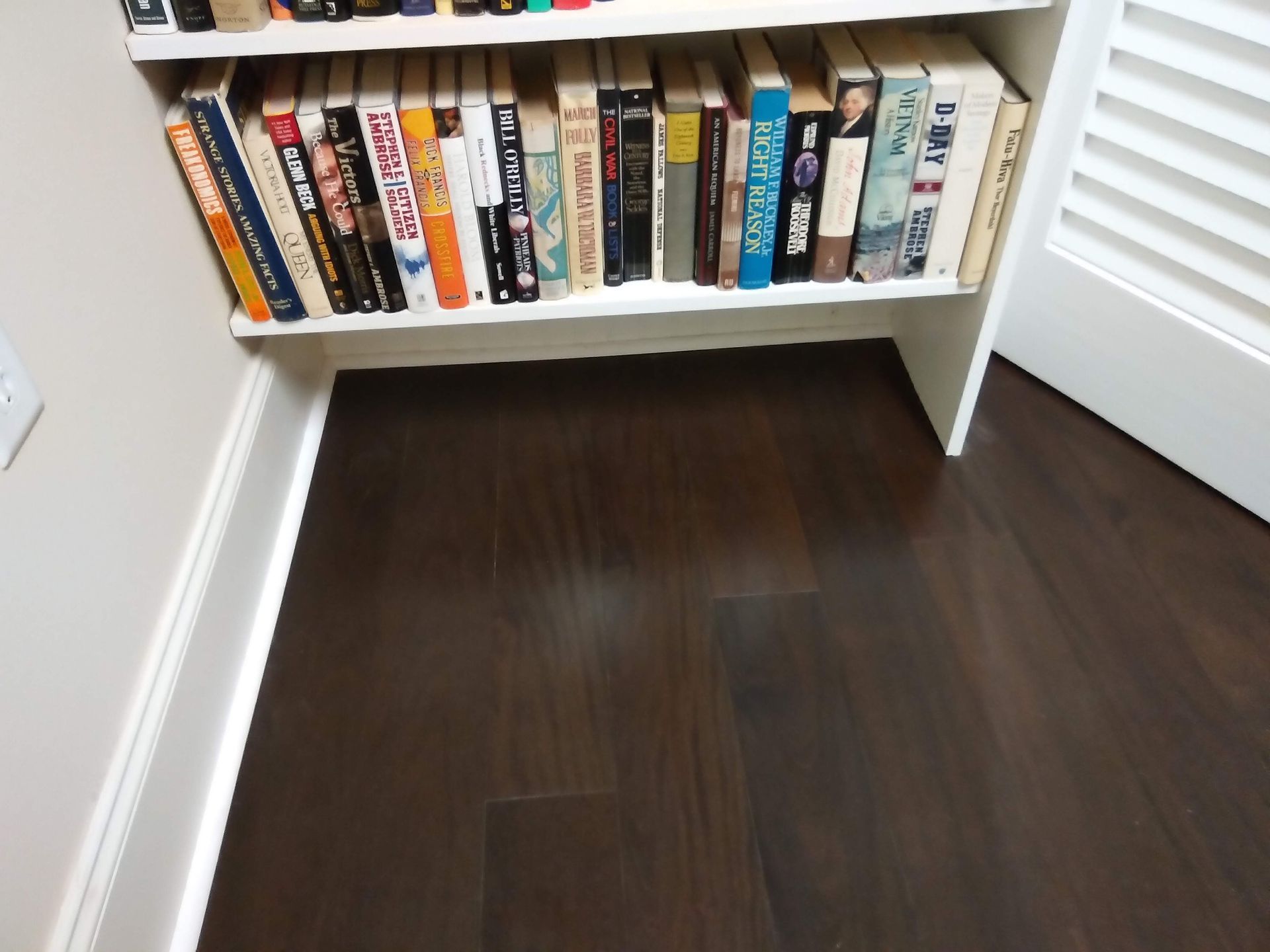 Bookshelves in a corner of a room with books on a dark wood floor