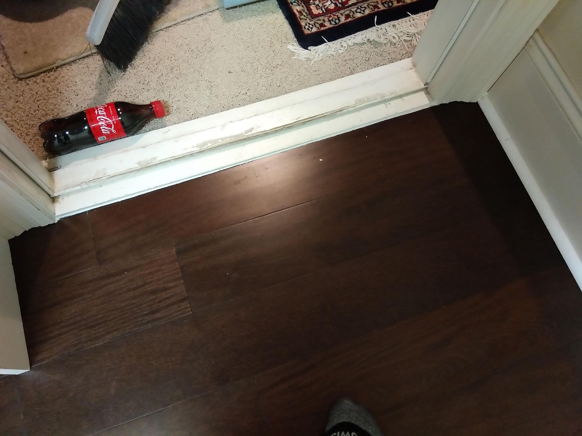 A doorway with a dark wood floor and a red soda bottle on a carpeted threshold.