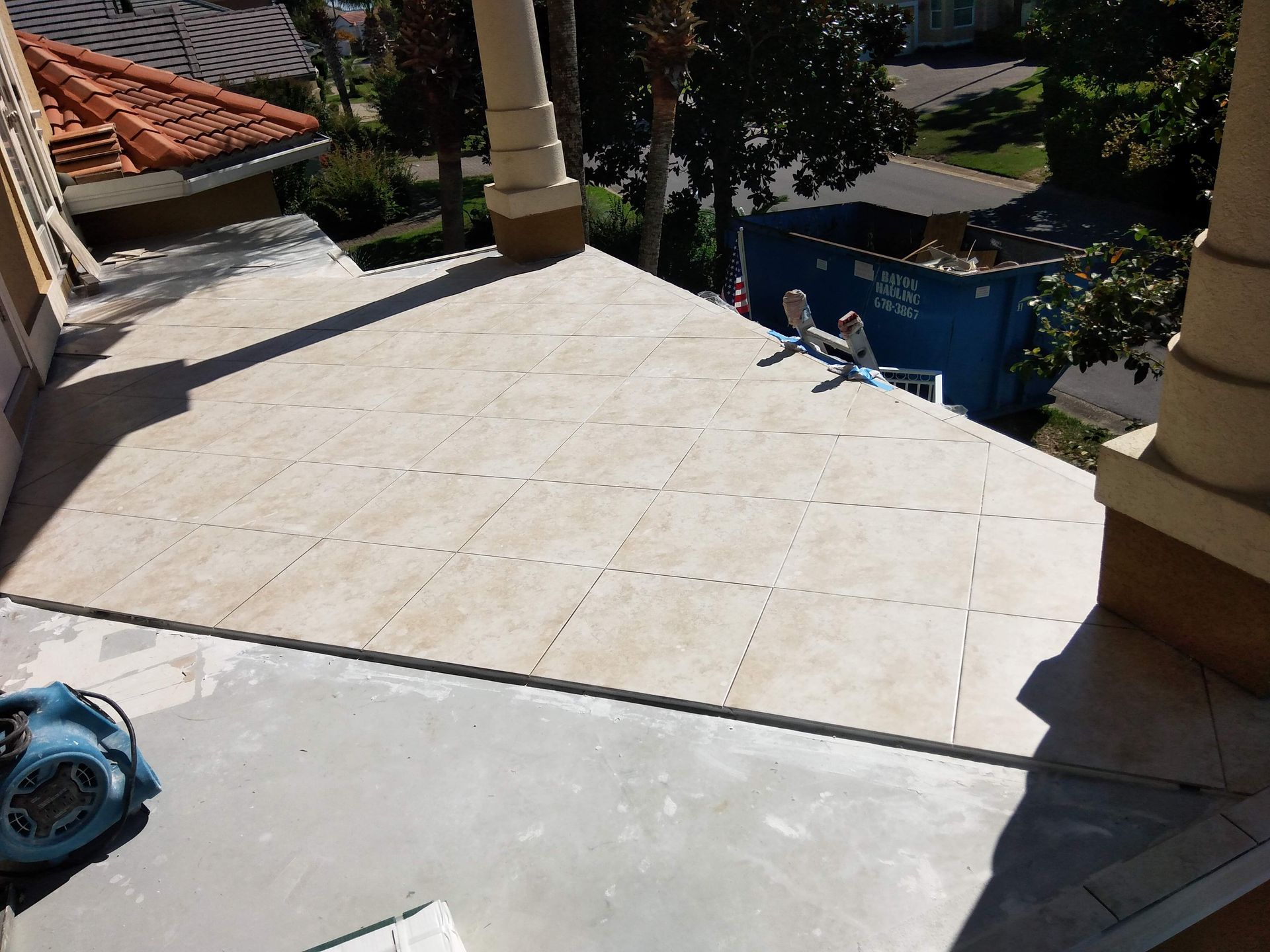Sunlit tiled patio overlooking a pool, with a blue toy and columns in the foreground.