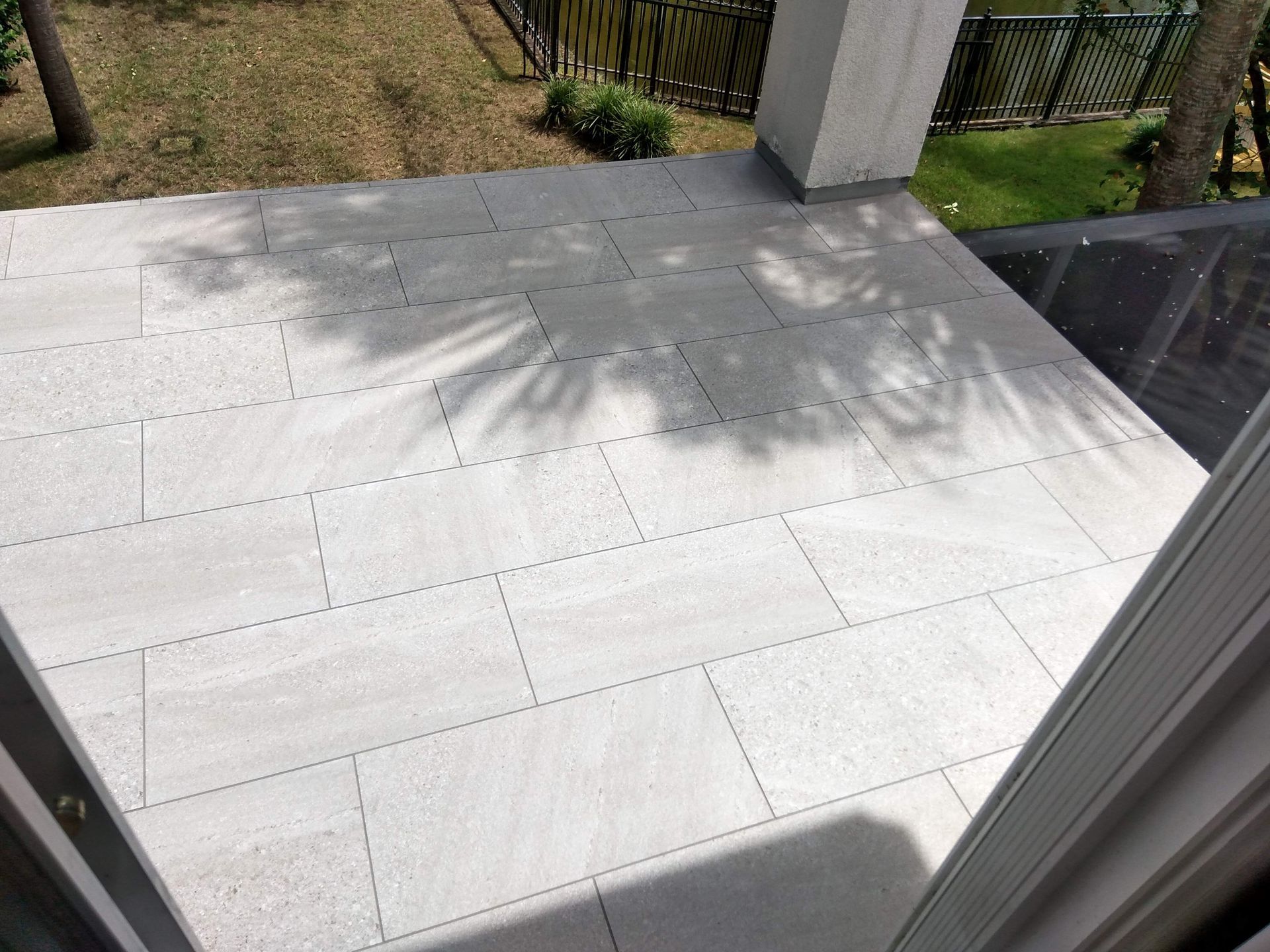 White tiled patio with shadows from a tree, next to a porch and yard fence.