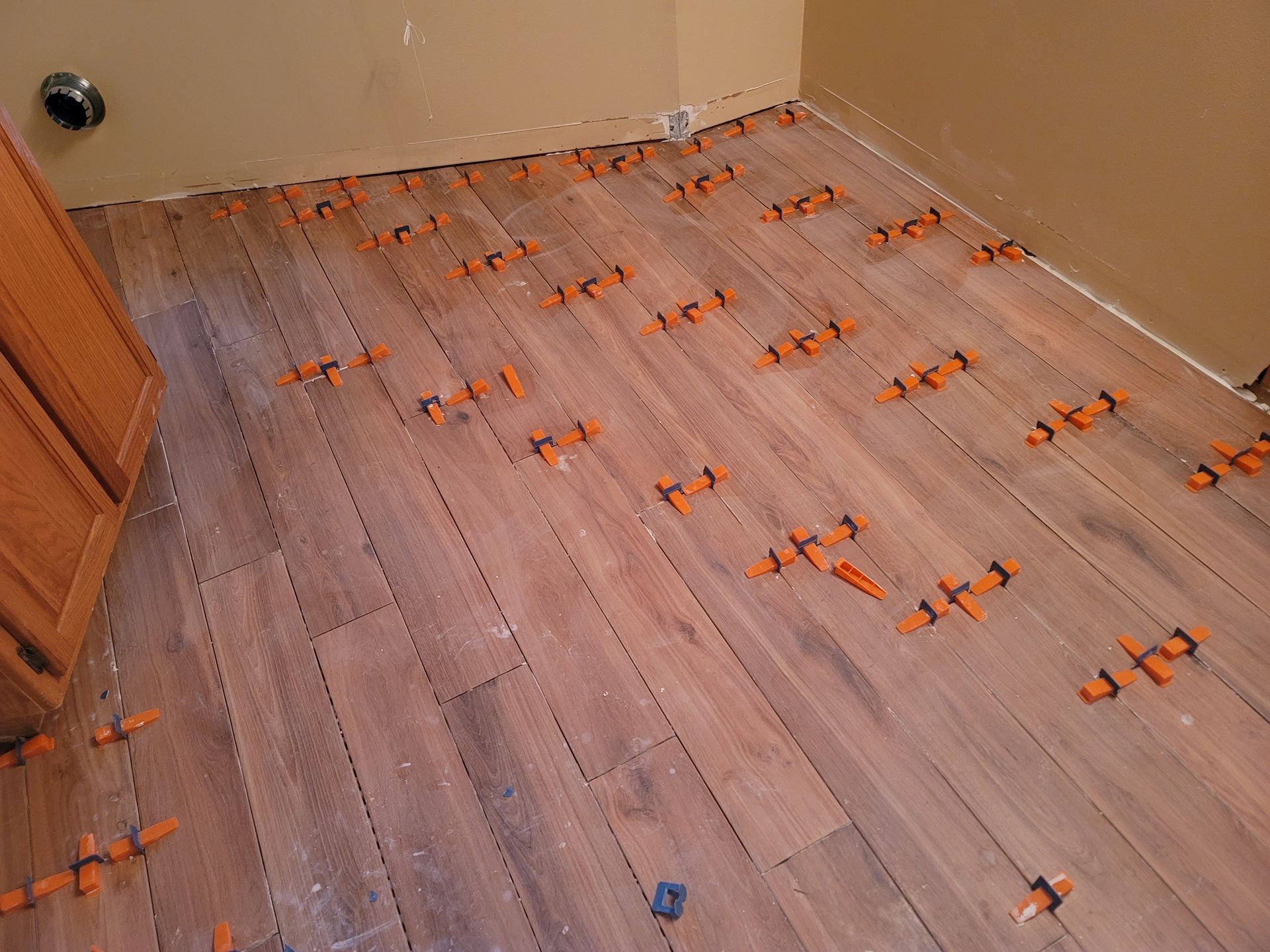 Wood floor under construction with orange tile spacers and beige walls in a room corner