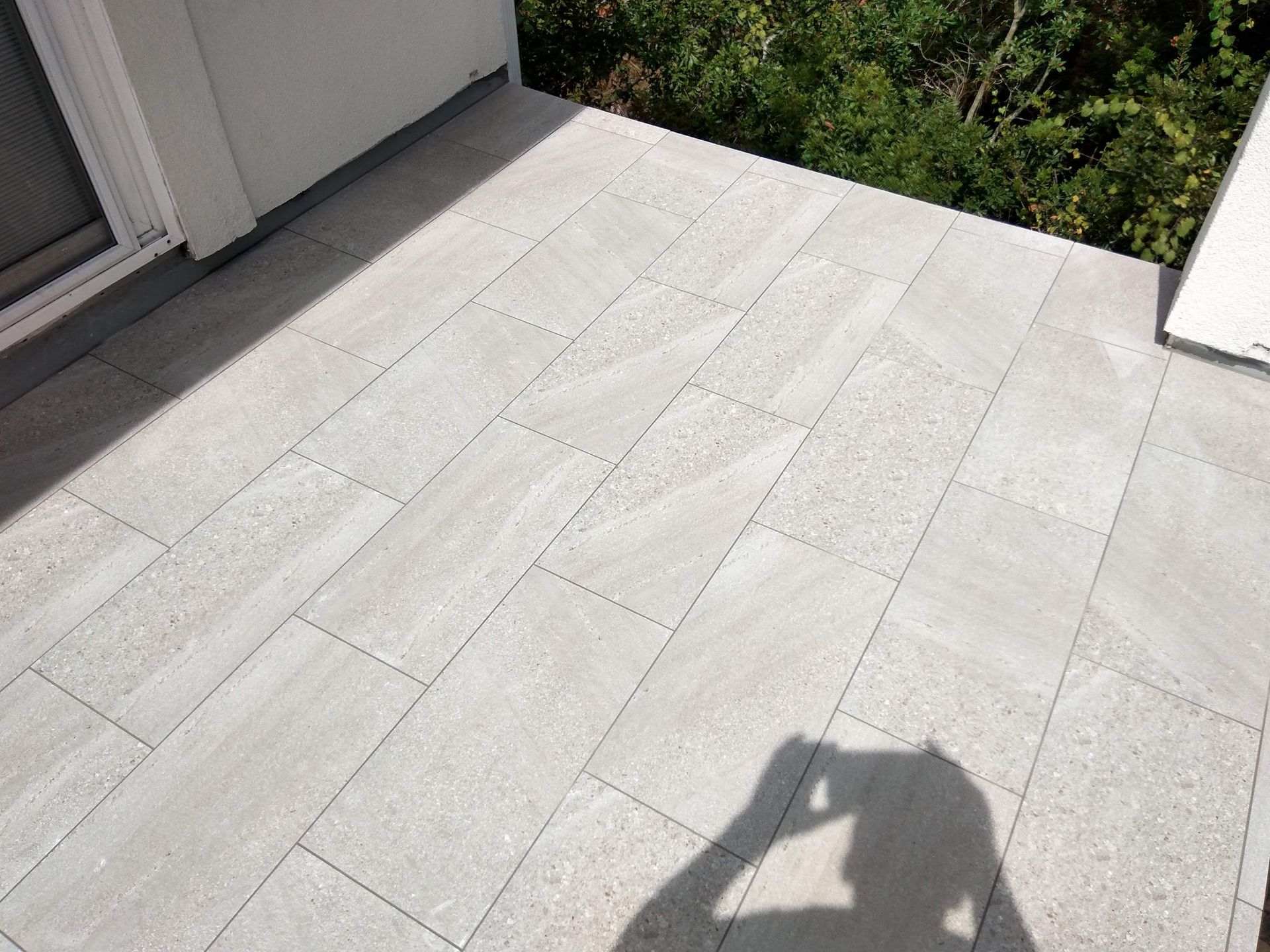 Sunlit white stone patio beside a house, with shadows and greenery at the edge