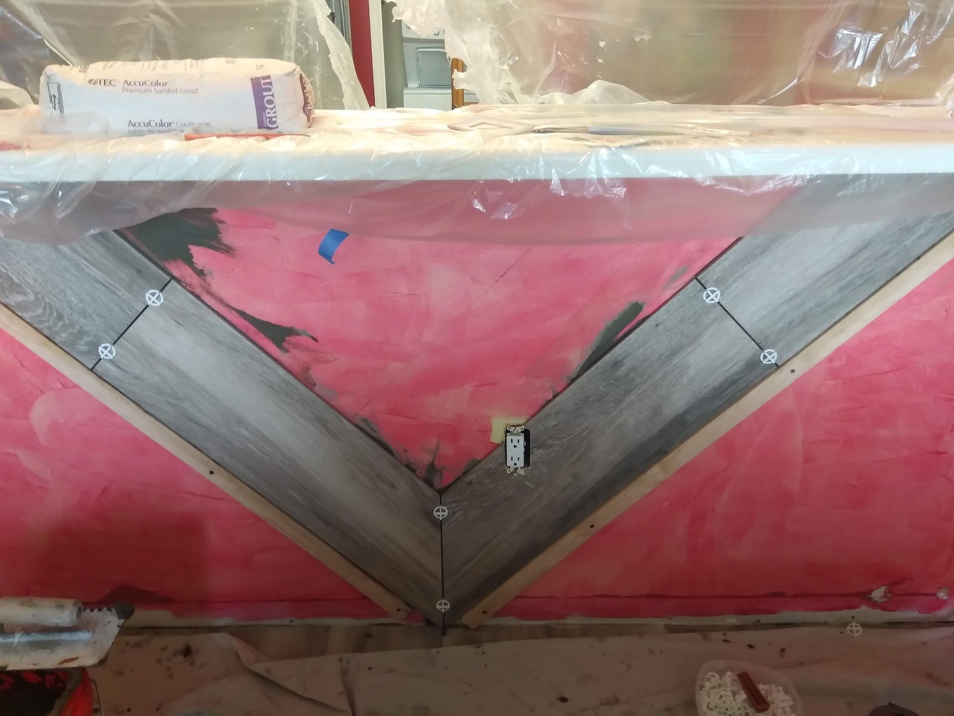 Pink wall with a large gray V-shaped painted design and visible tape or hardware in the center