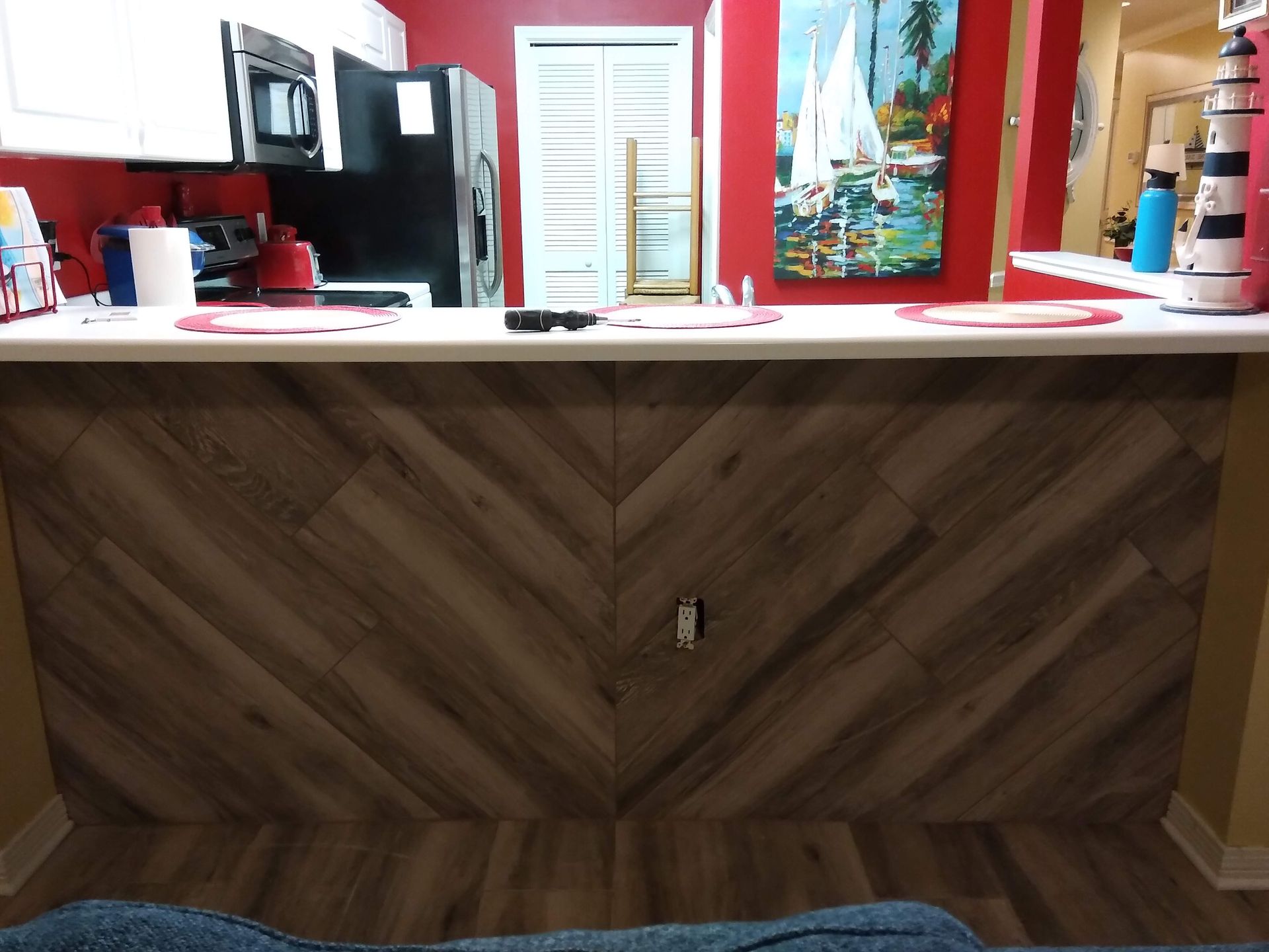 Kitchen island with chevron wood paneling, white countertop, and red-walled kitchen behind it
