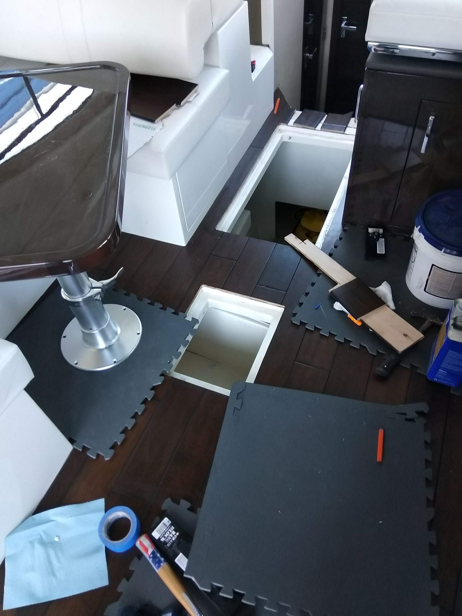 Cluttered room with broken black flooring tiles, a chair, and scattered boxes and tools