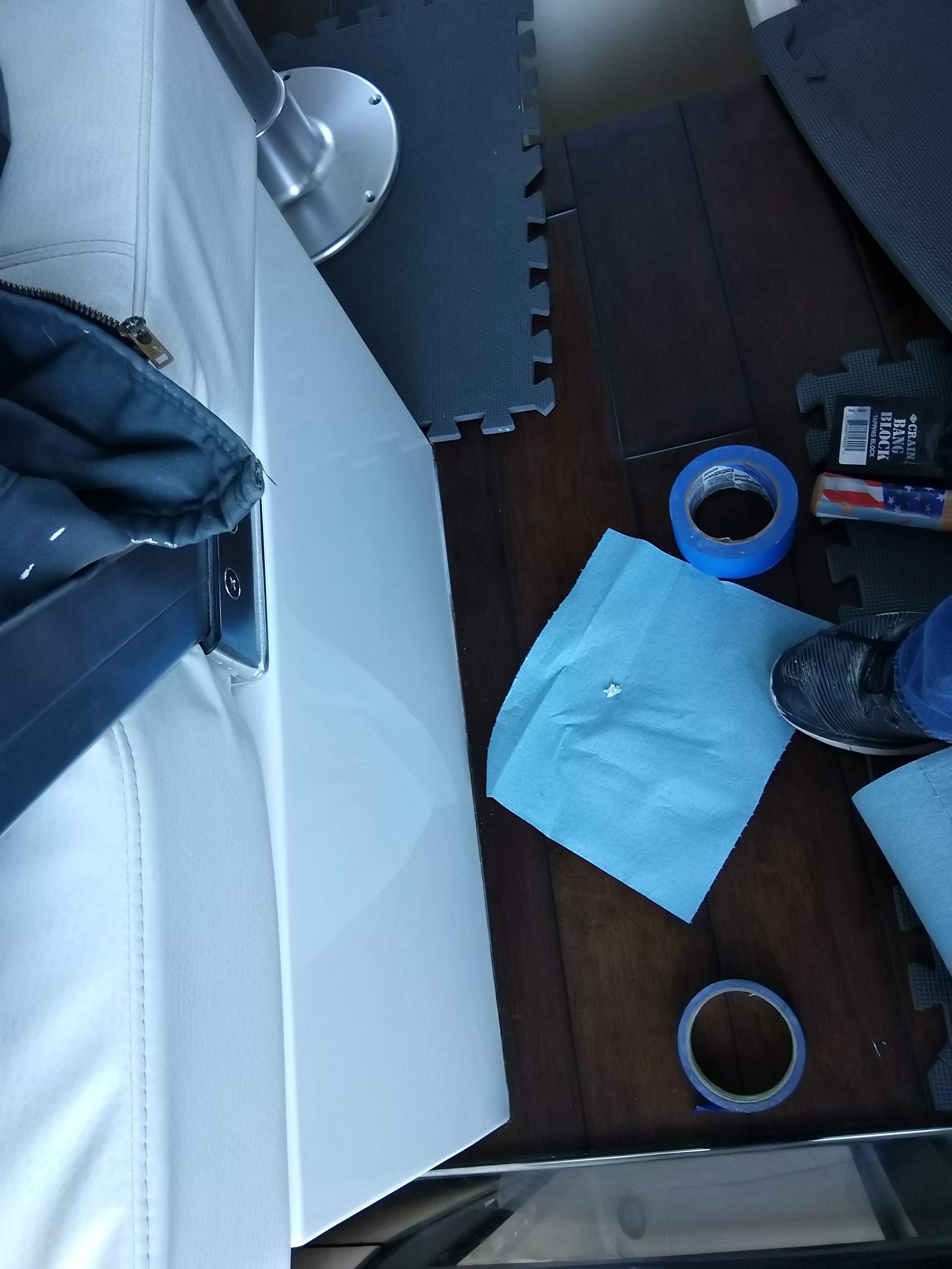 Cluttered tabletop with a blue cloth, tape rolls, scissors, and papers on a wooden floor