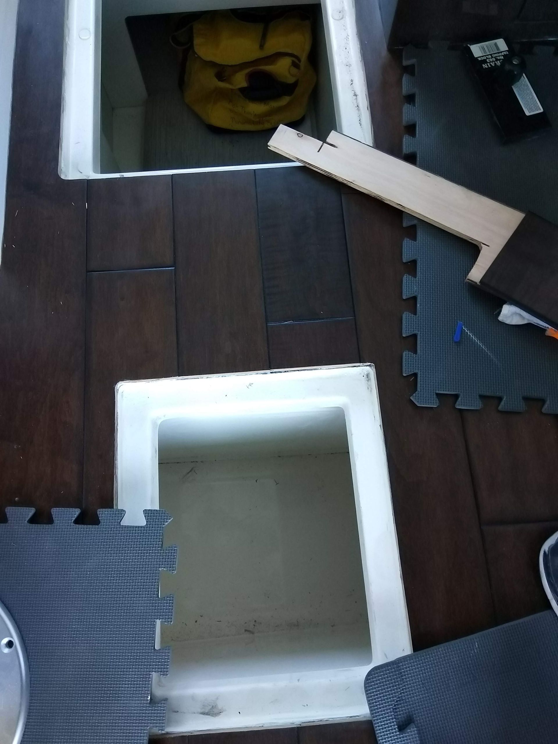 Scattered foam floor mats around an open white storage bin on dark wood flooring