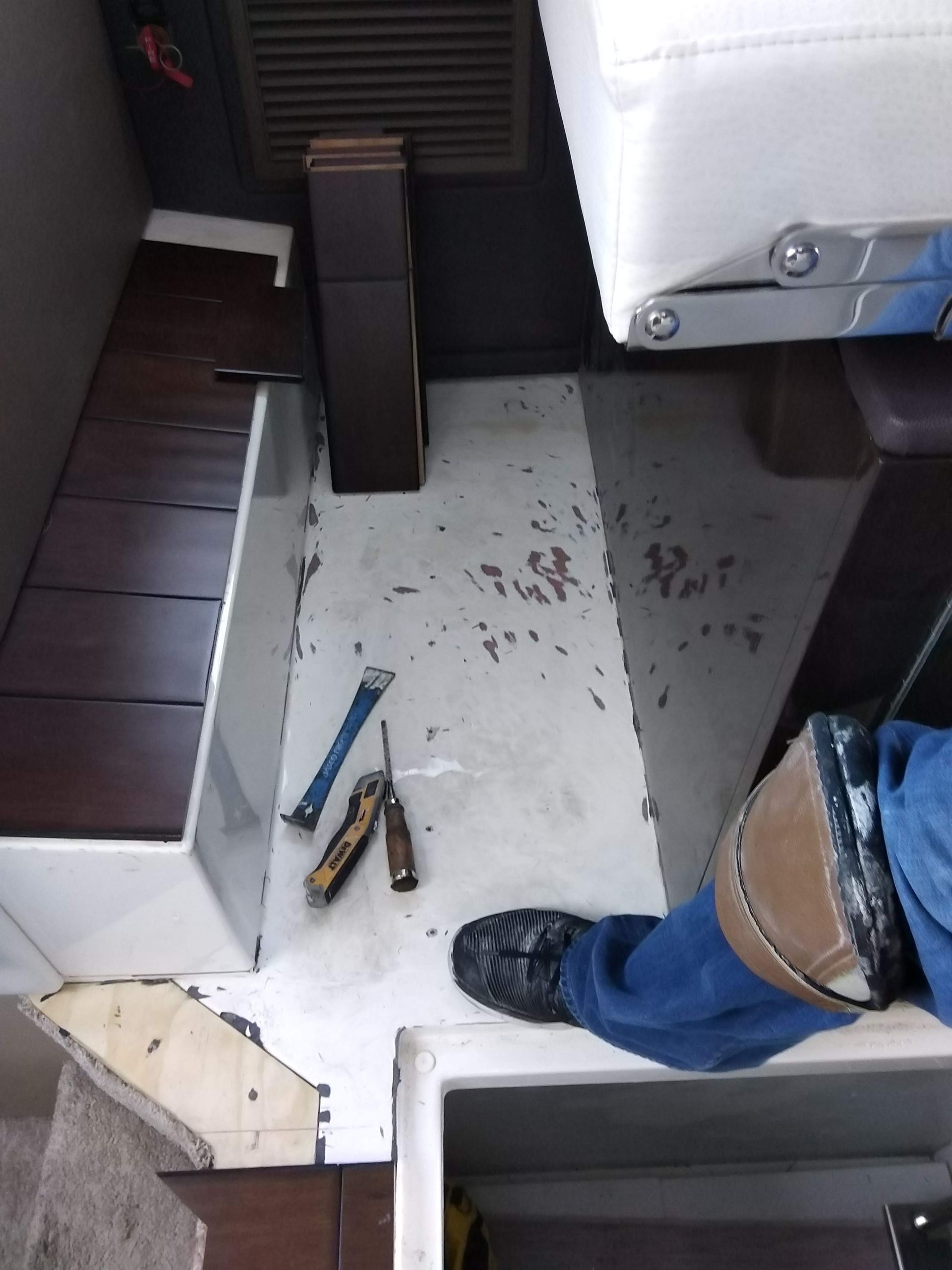 Work area with white floor panel, tools, and a person’s leg in jeans and black shoe.