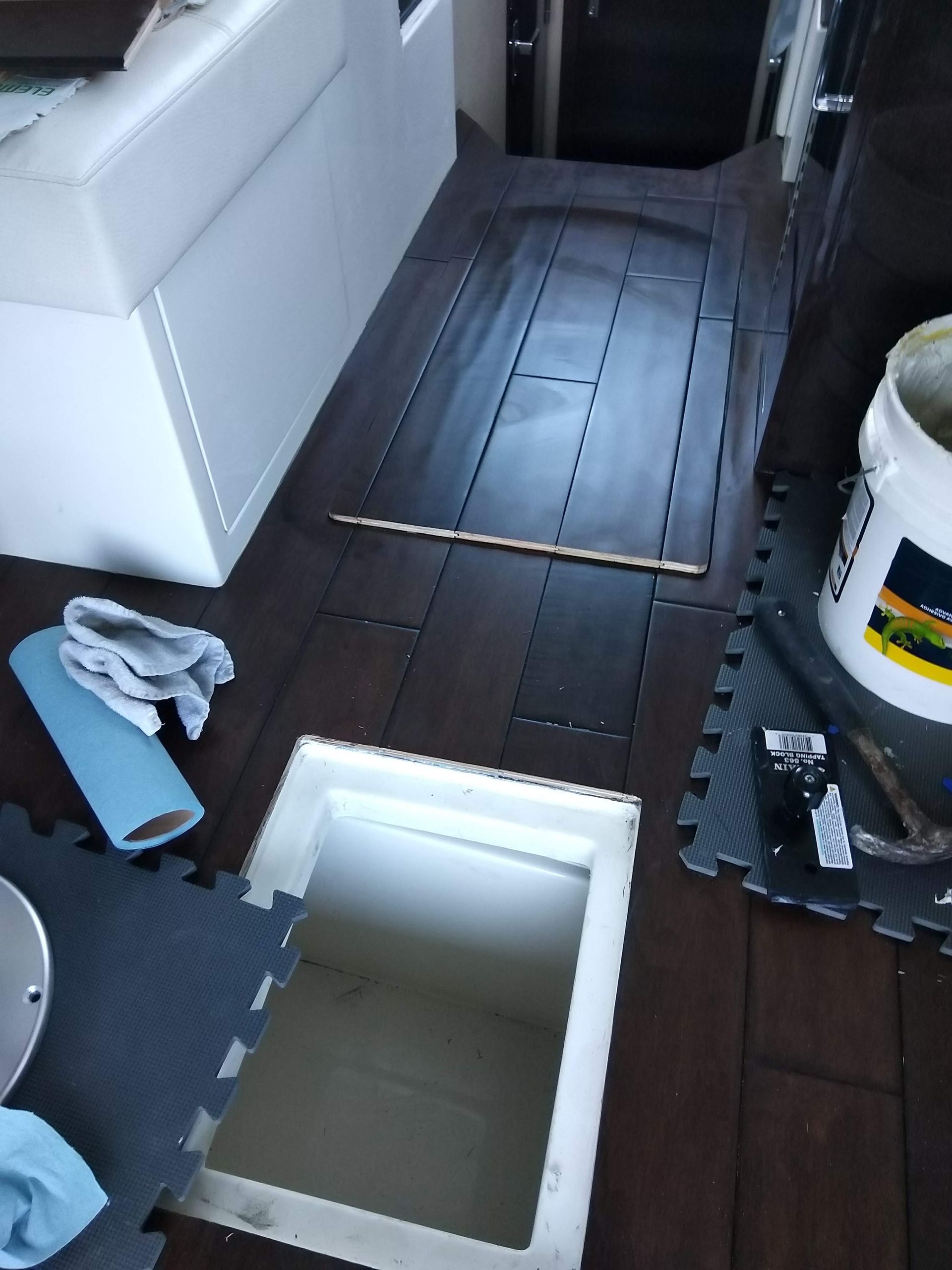 Dark wood floor with an open floor hatch, white sofa, cleaning cloths, and a paint bucket nearby