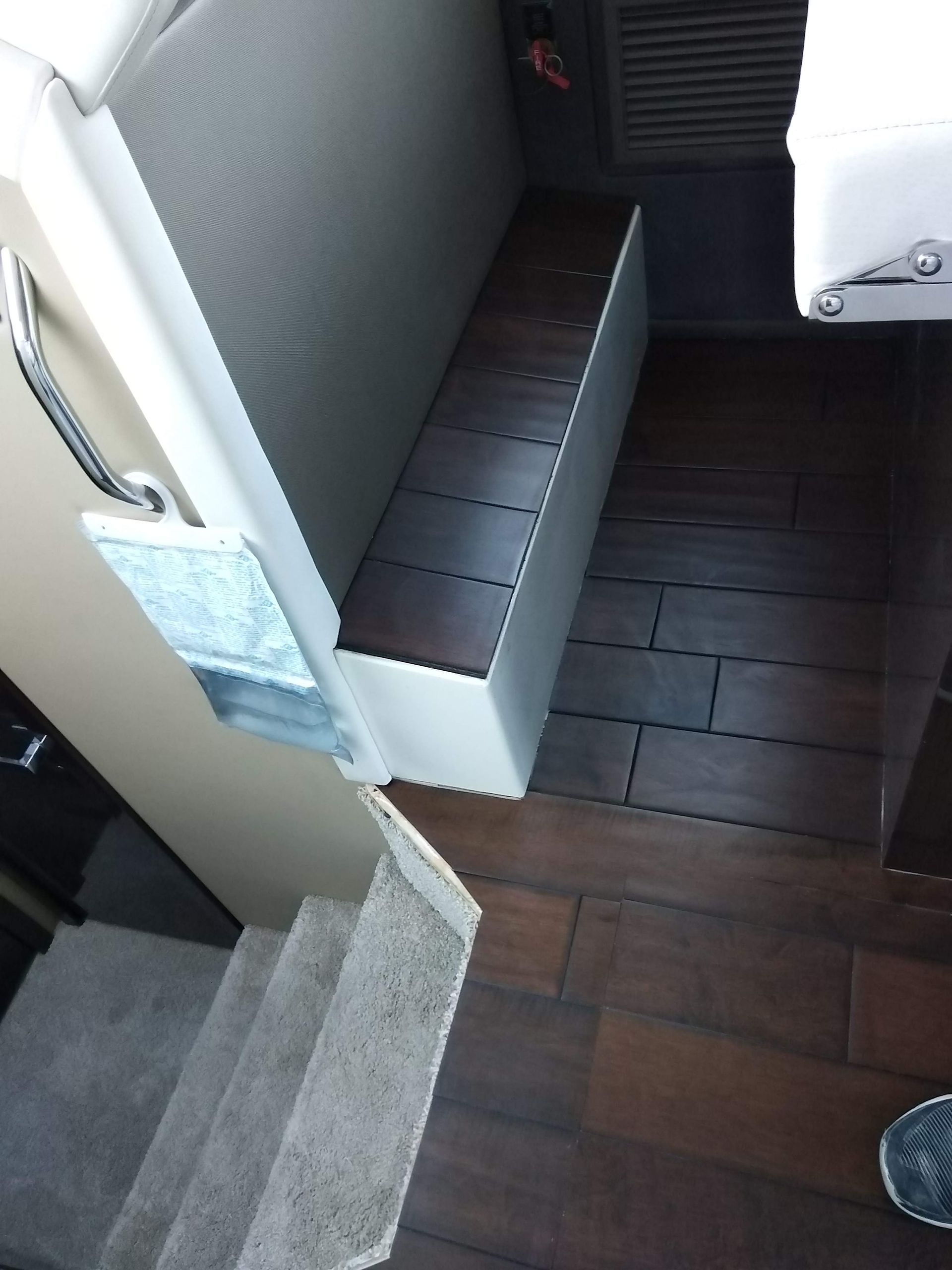 Indoor stair landing with gray steps, white wall, and dark wood floor beside a narrow bench or shelf unit