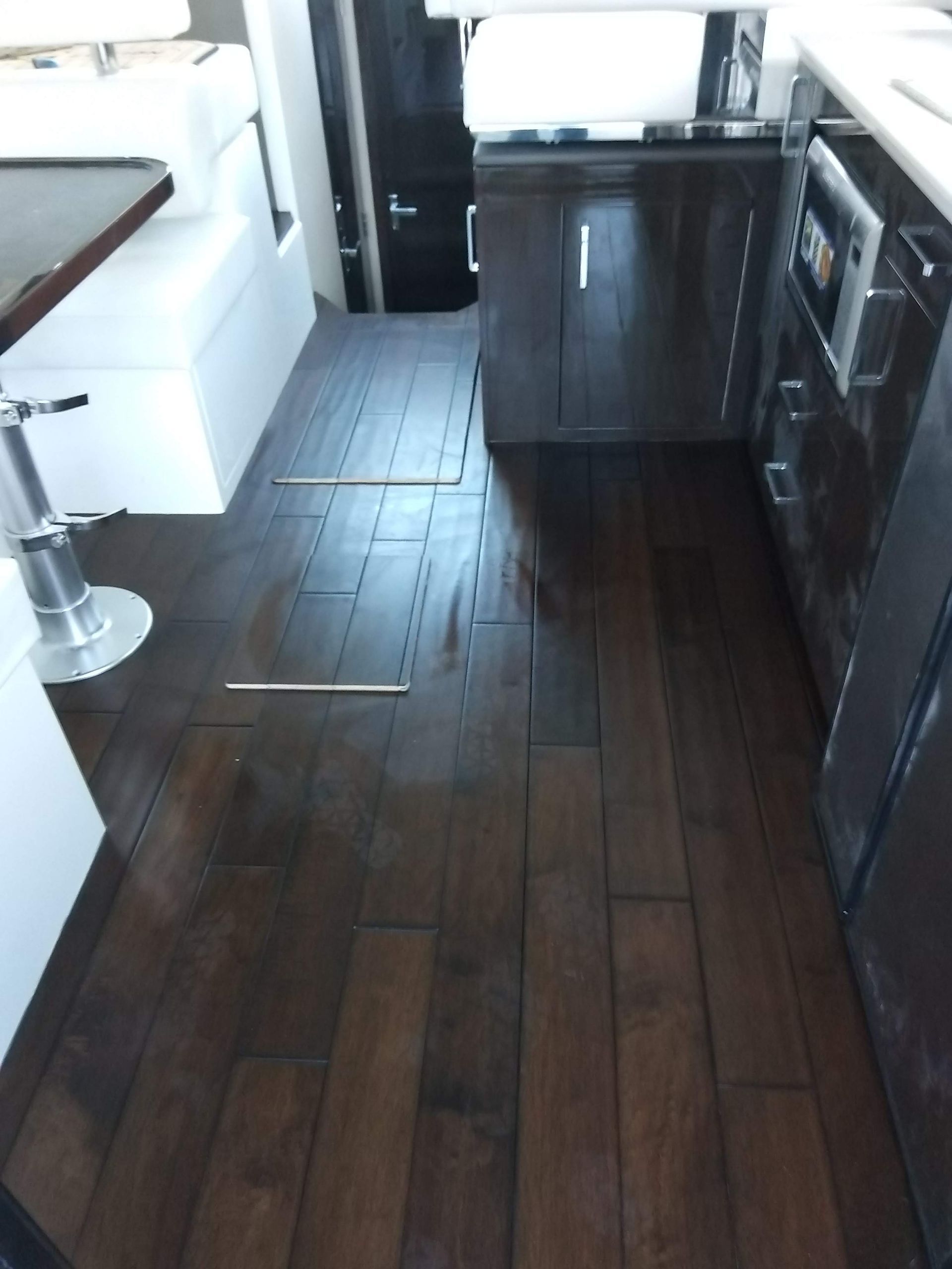 Narrow kitchen aisle with dark wood floors, white cabinets, and a sink counter on the right.