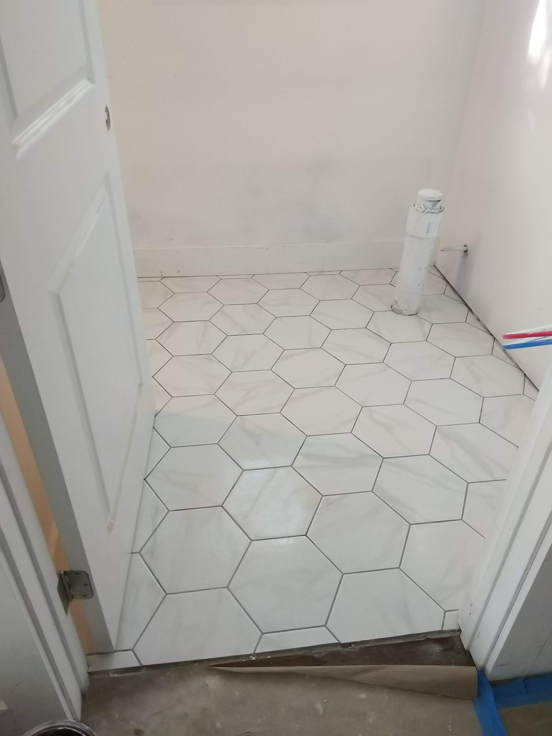 Small white-tiled bathroom with a toilet paper roll on the floor and an open door.
