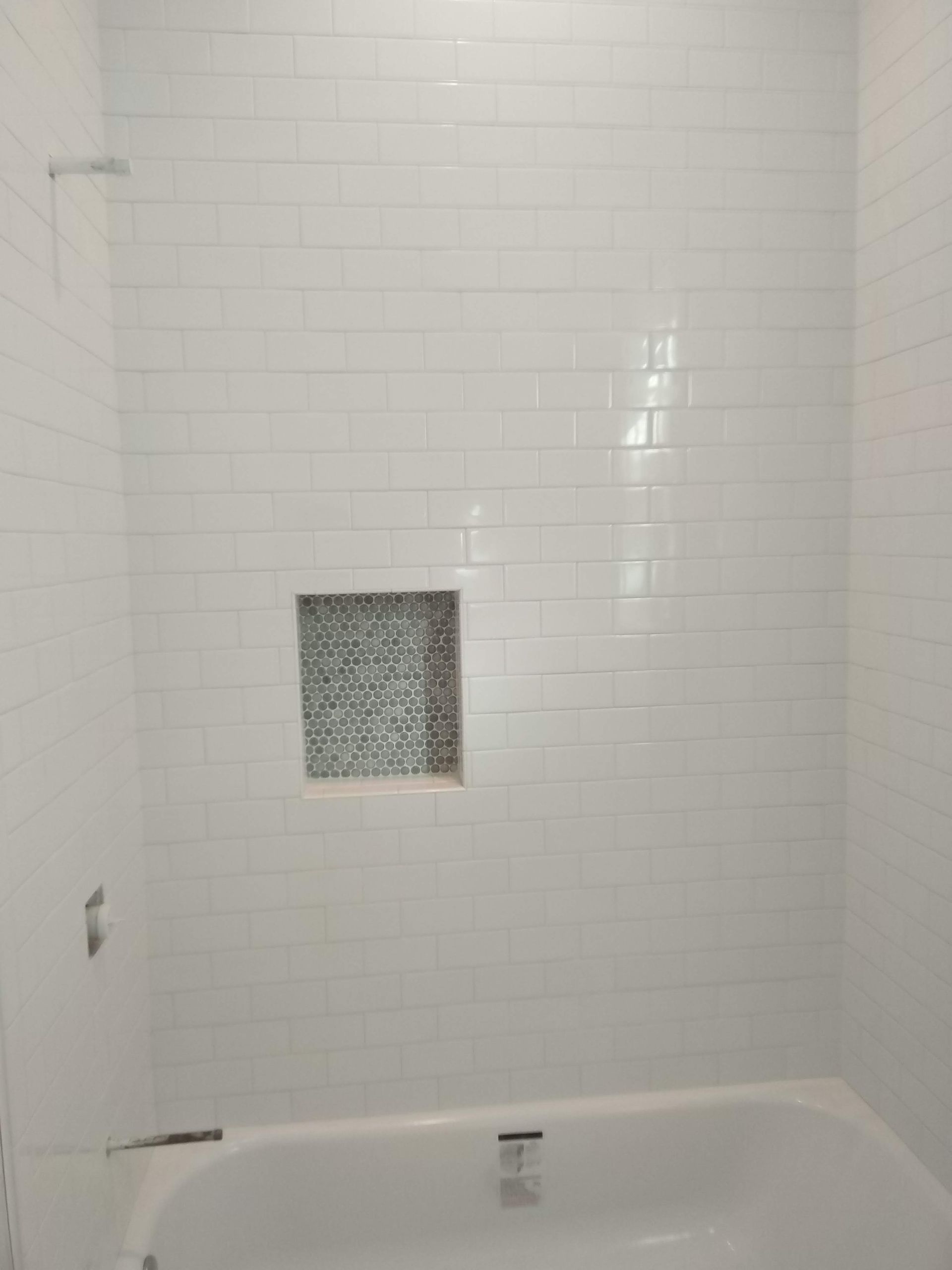 White tiled shower with a small square glass-block window and tub edge visible below.