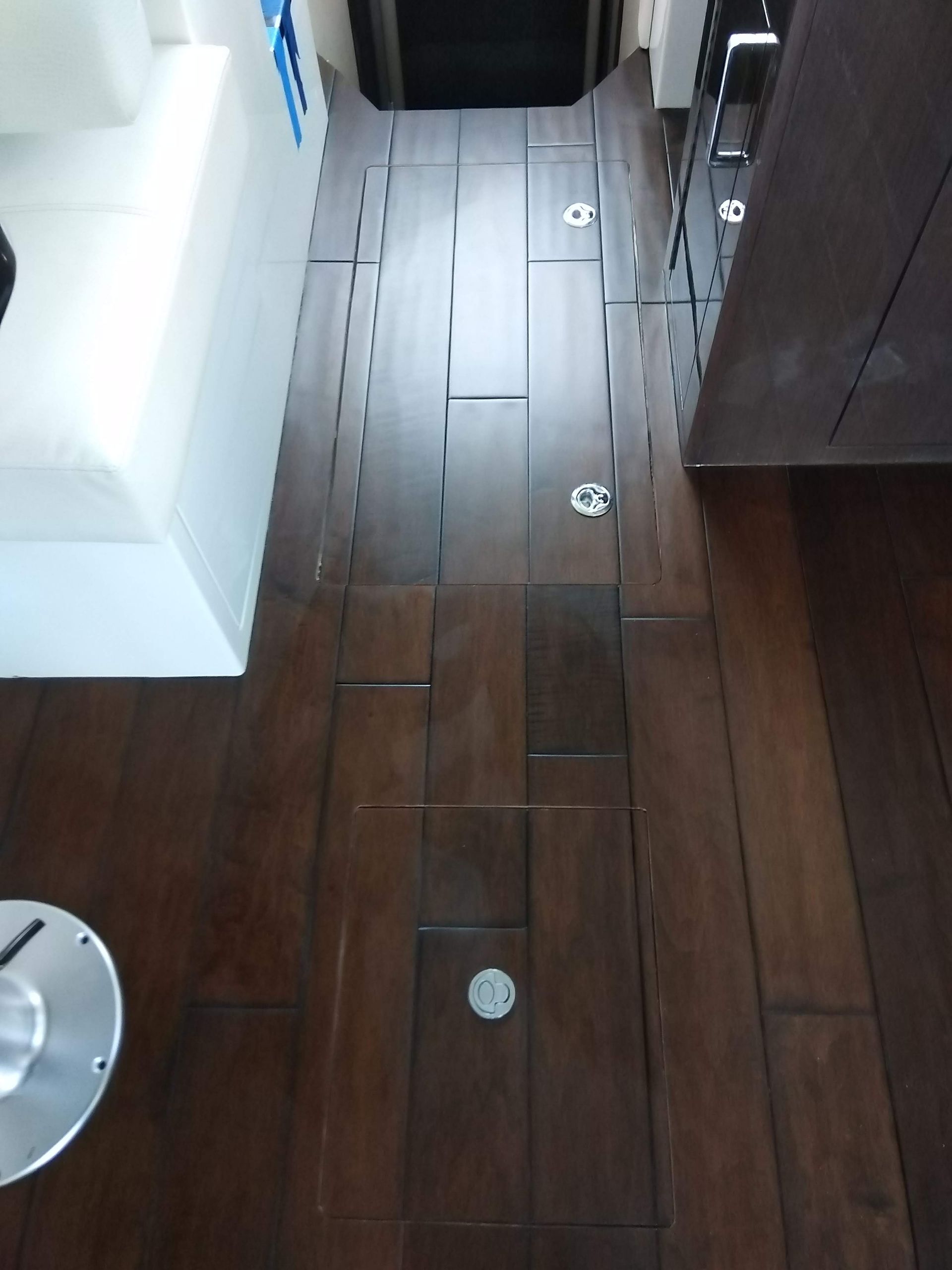 Wooden floor with round floor lights, next to a white sofa and dark cabinetry in a narrow hallway