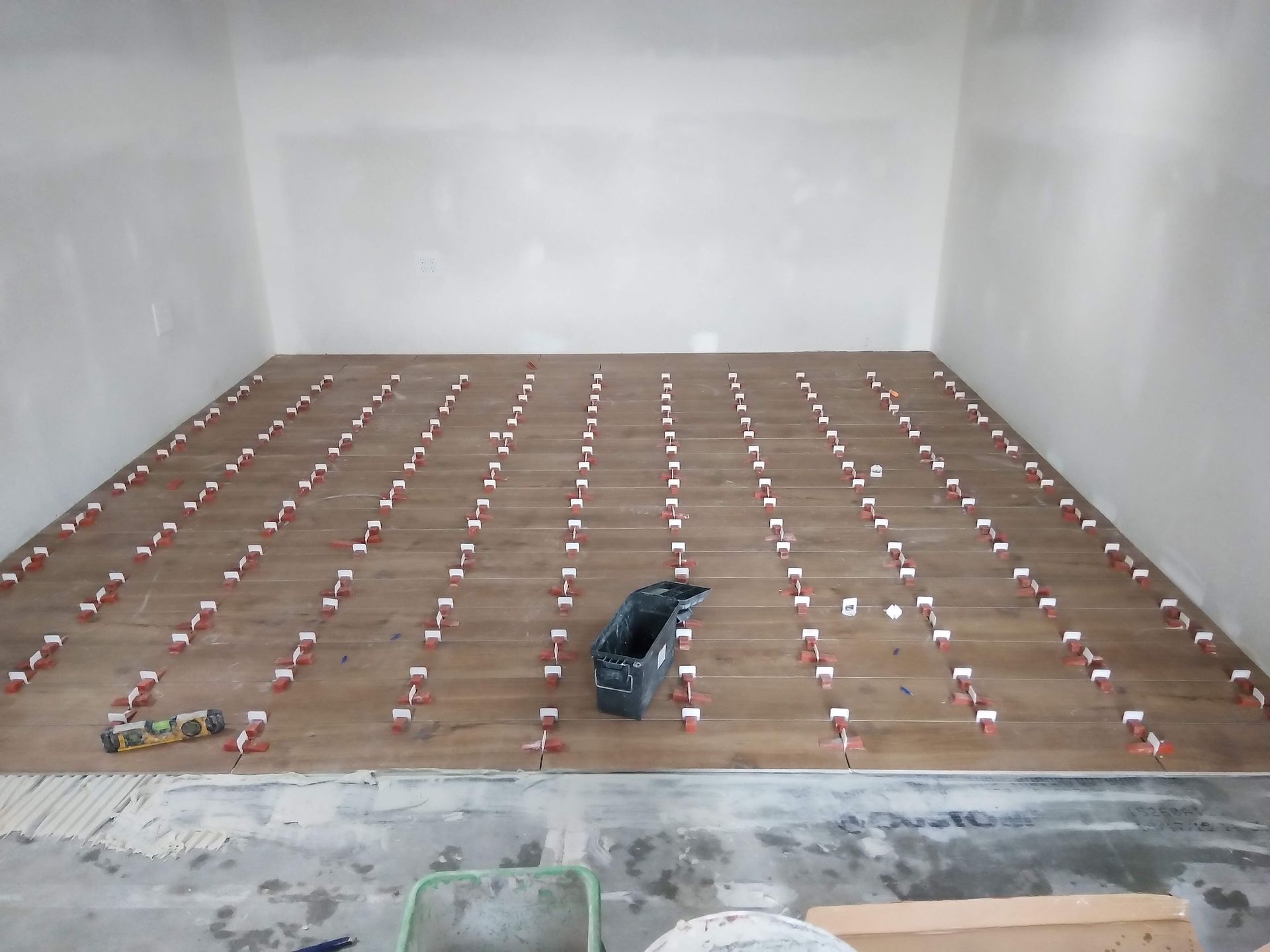Large empty room with a wooden floor covered in rows of small red-and-white objects and one dark tarp in the center