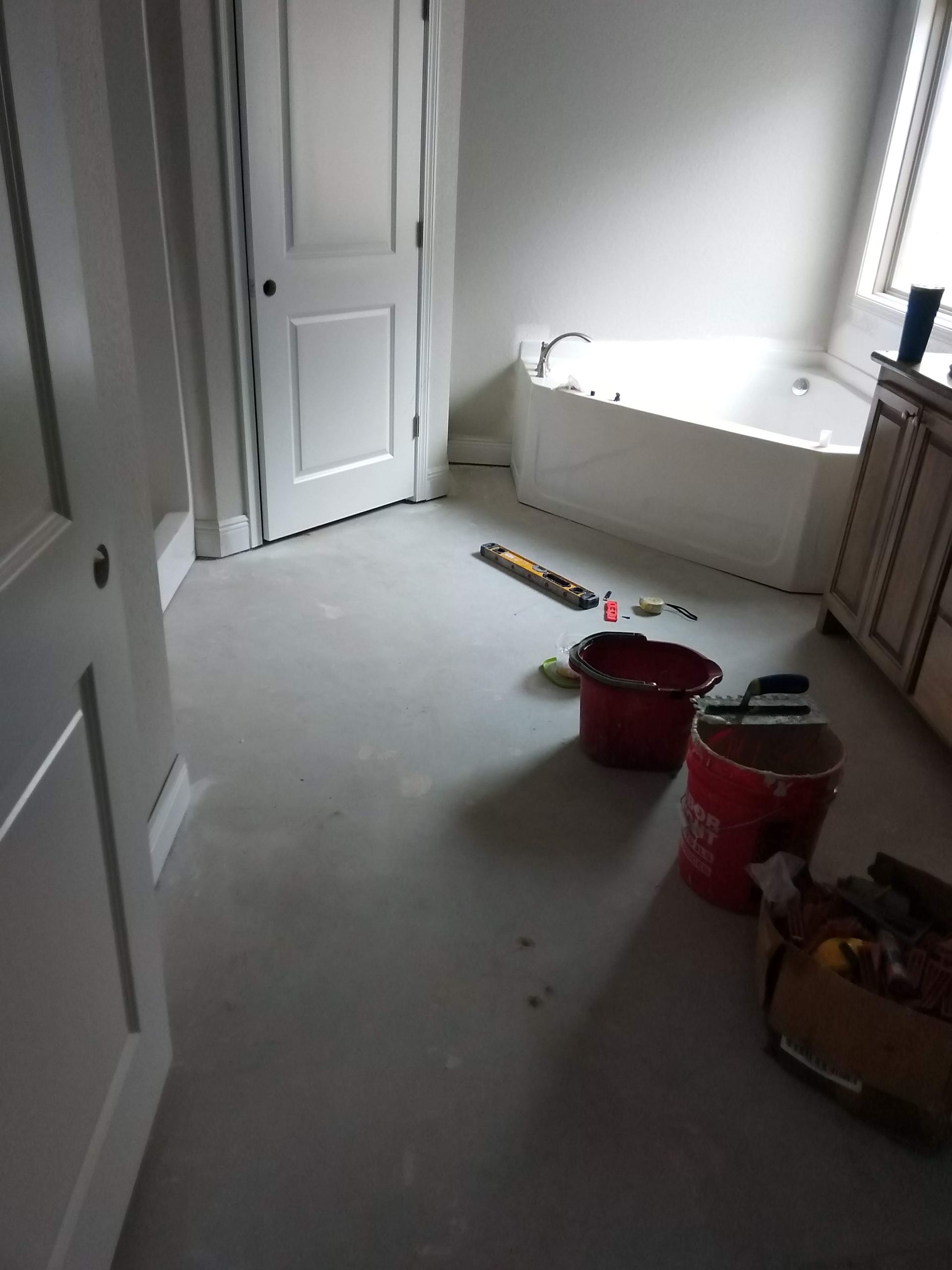 Unfinished room with white walls, window, paint buckets, tools, and debris on the floor.