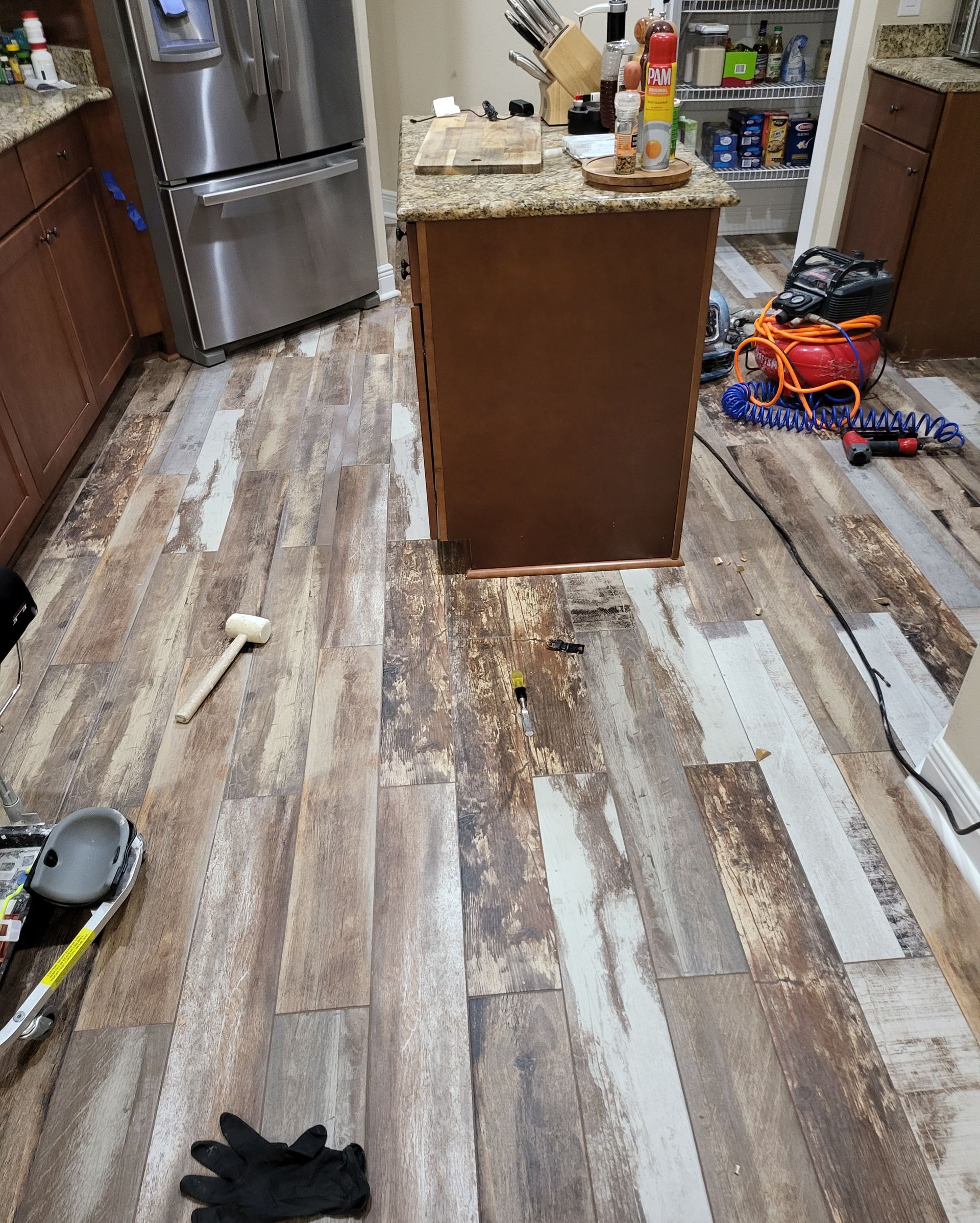 Kitchen with partially installed wood-look flooring, central island, and cleaning tools scattered on the floor.