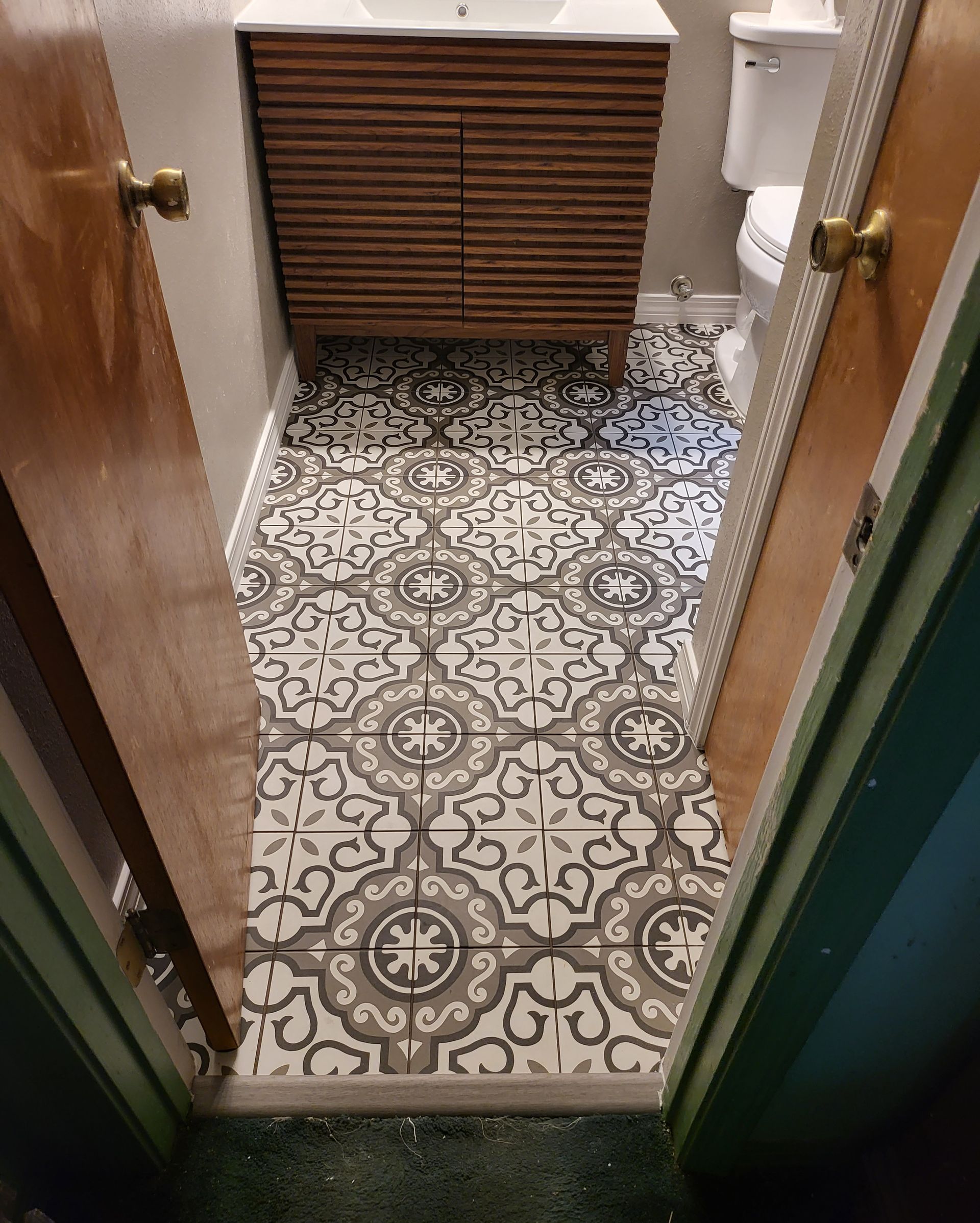 Narrow hallway with patterned tile floor, open wooden doors, and a radiator at the end.